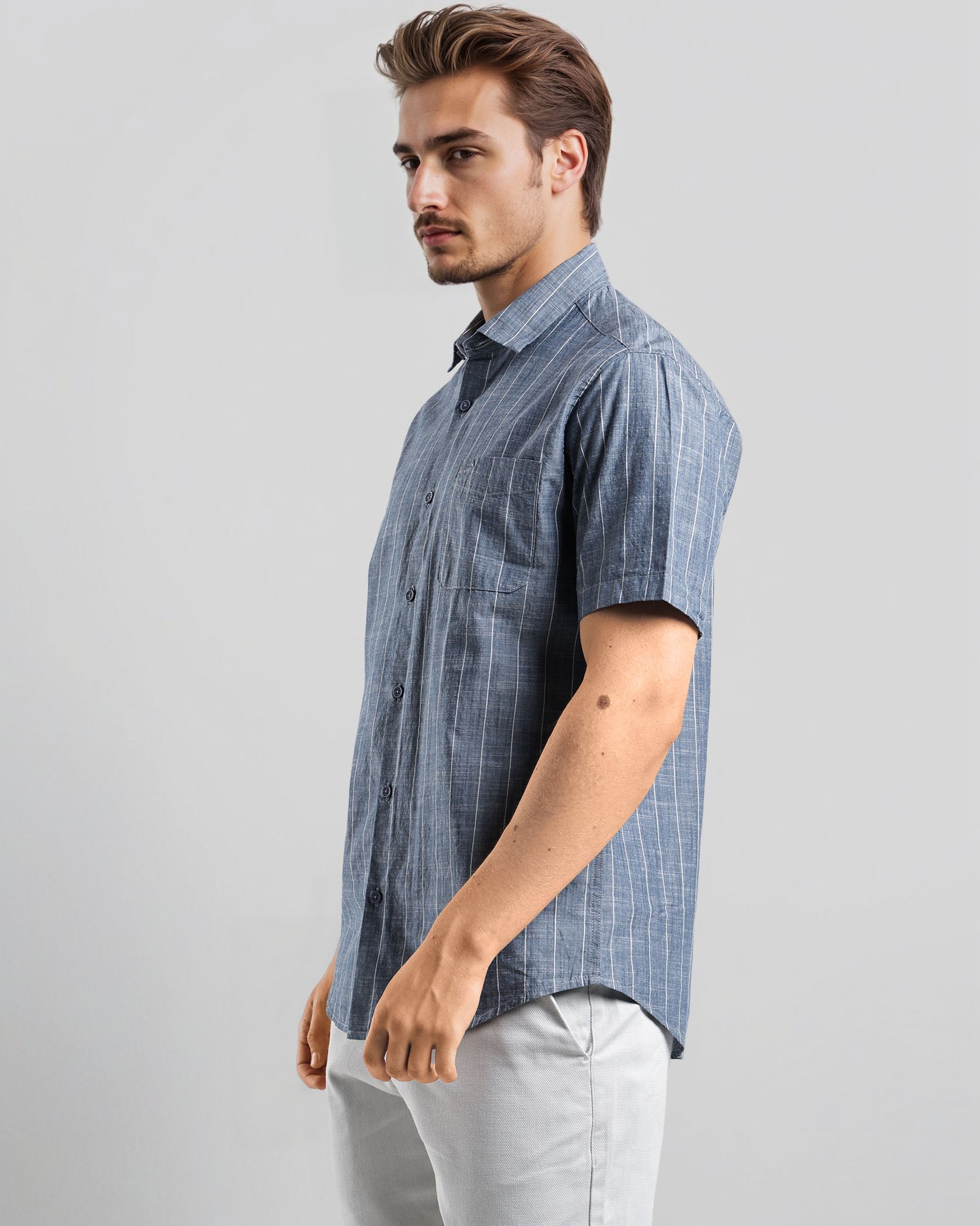 Man wearing a blue checkered shirt and light gray pants on a white background