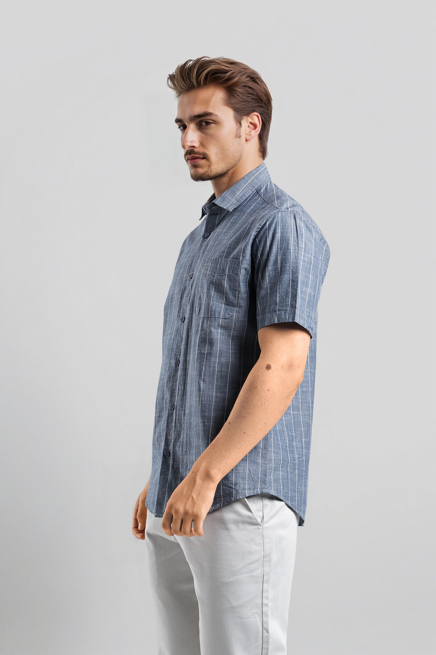 Man wearing a blue checkered shirt and light gray pants on a white background