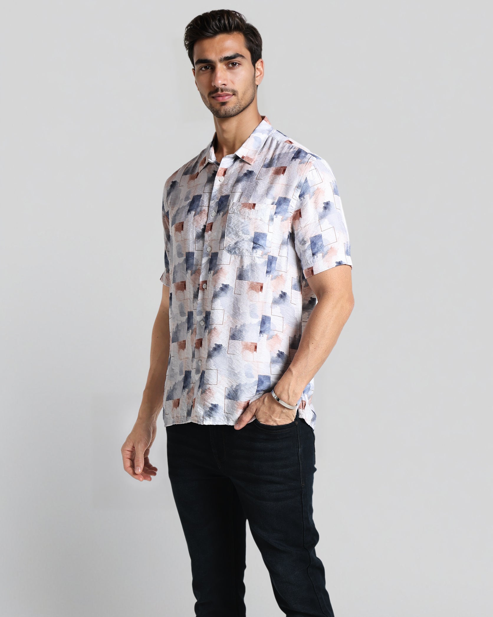 Man wearing a patterned shirt and black pants on a plain background