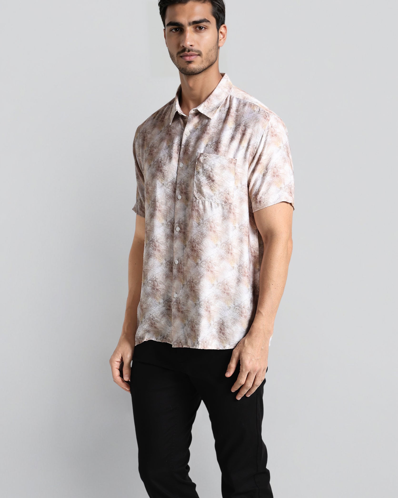 Man wearing a patterned shirt and black pants on a gray background