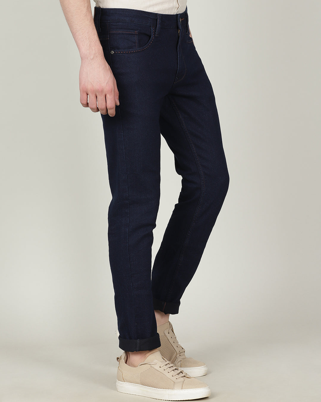 Man wearing a blue dark blue solid mid rise slim tapered jean on a light gray background