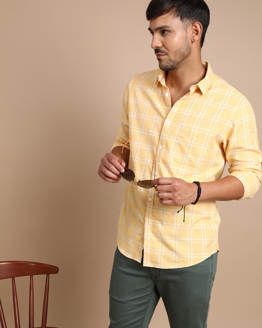 Man wearing a yellow casual yellow checked full sleeve 100% cotton shirt with casual styling on a gray background