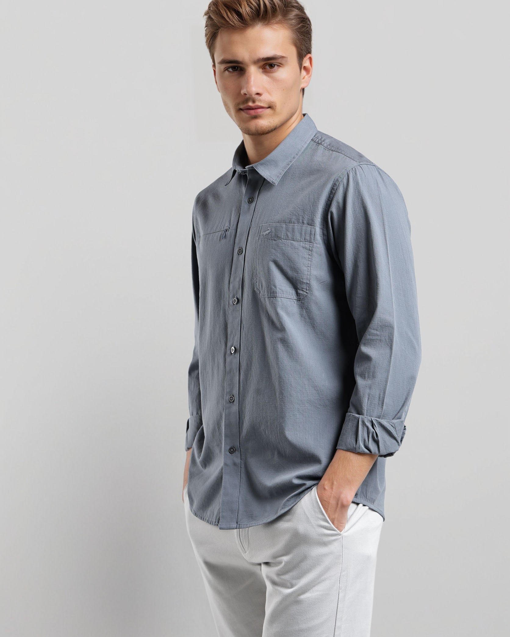 Man wearing a light blue button-up shirt and white pants on a gray background