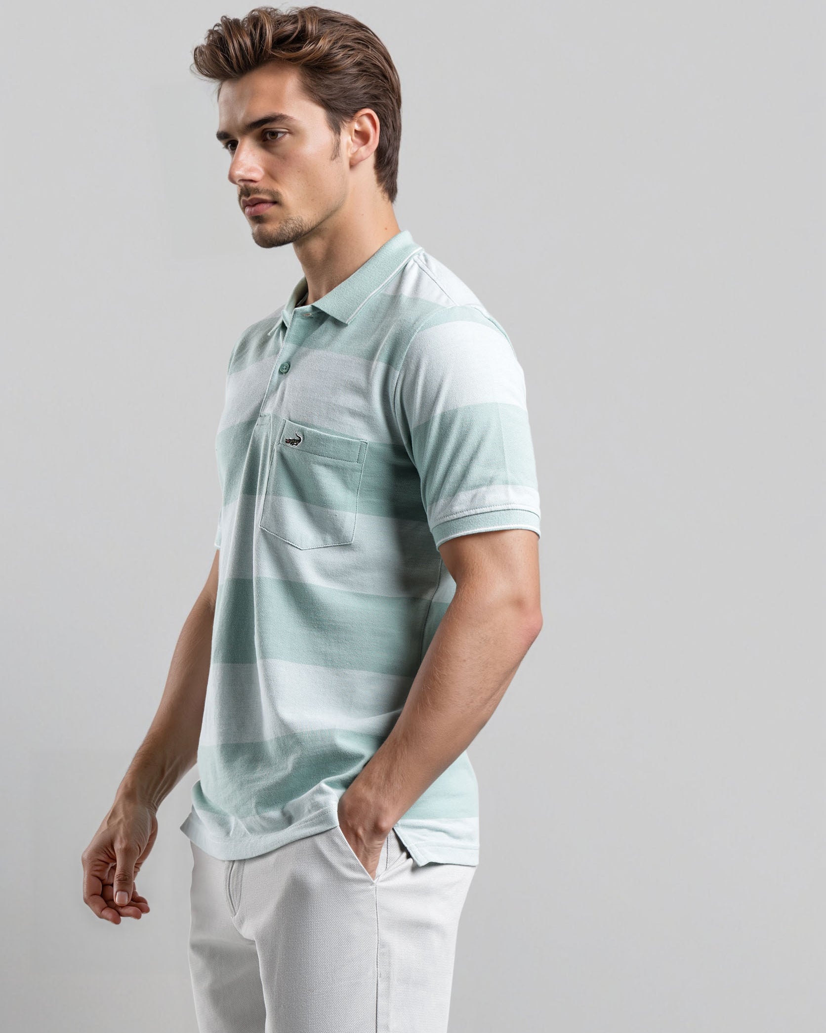 Man wearing a light green polo shirt and white pants on a gray background