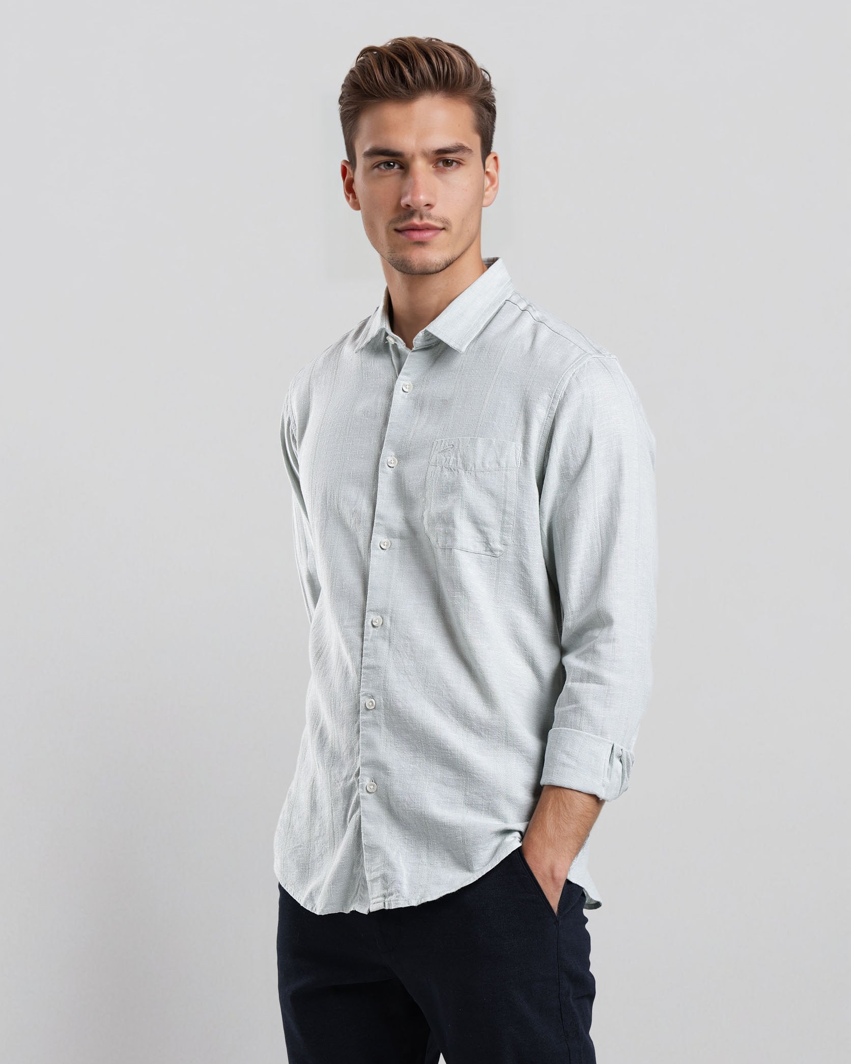 Man wearing a light gray button-up shirt and dark pants on a white background