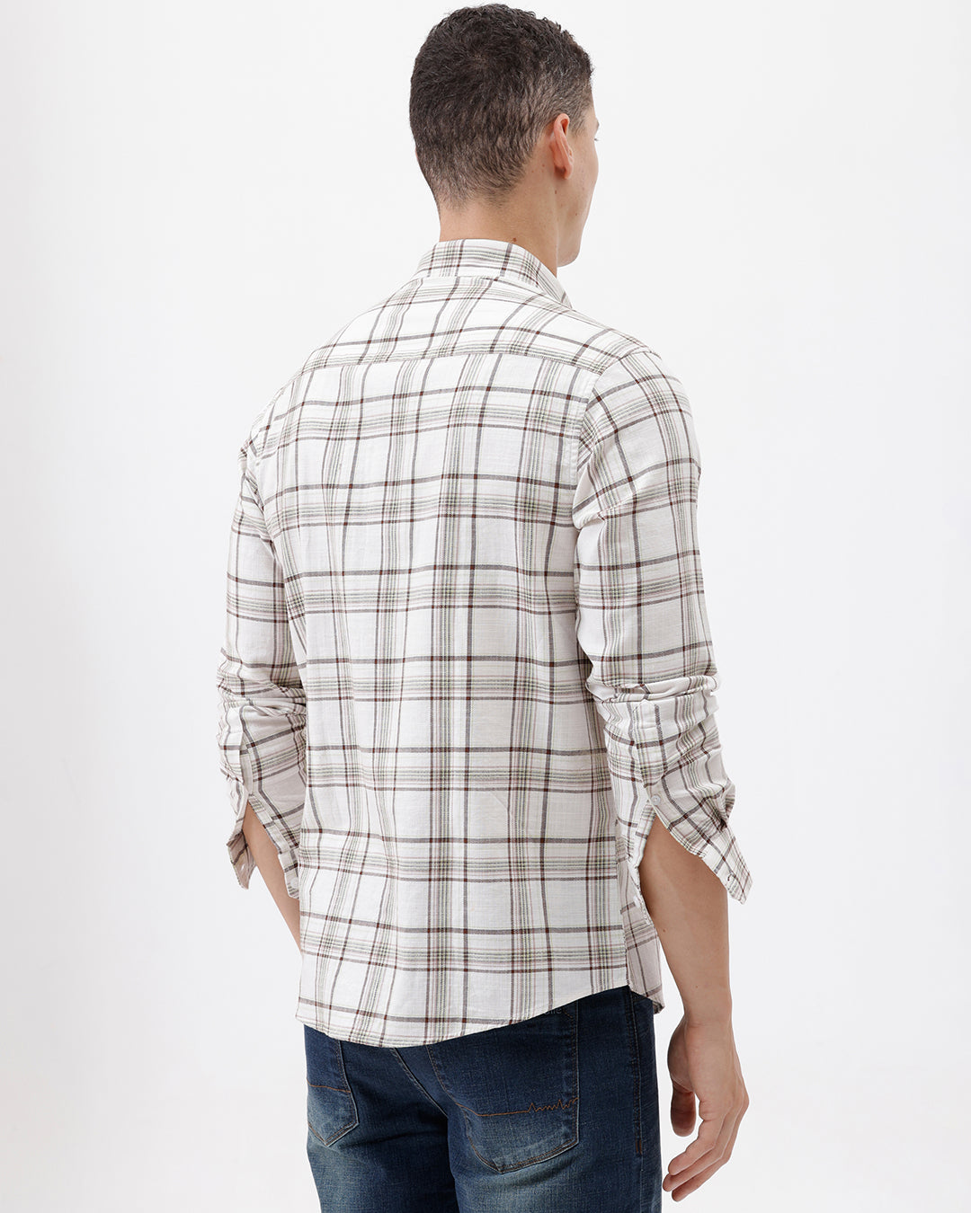 A man wearing a long-sleeve plaid button-up shirt in beige and brown with dark blue jeans, standing against a plain white studio background.