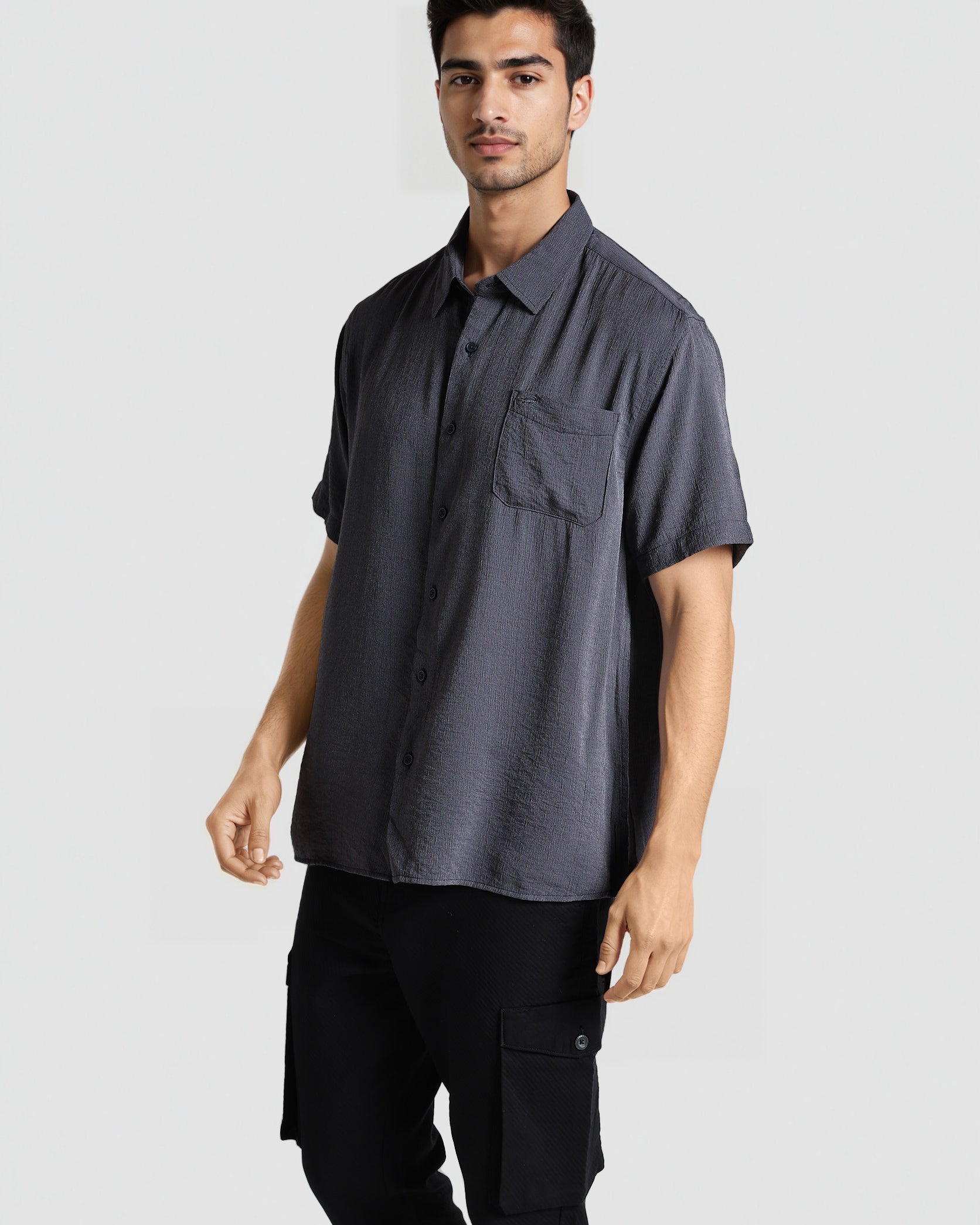 Man wearing a dark gray short-sleeve shirt and black pants on a light gray background