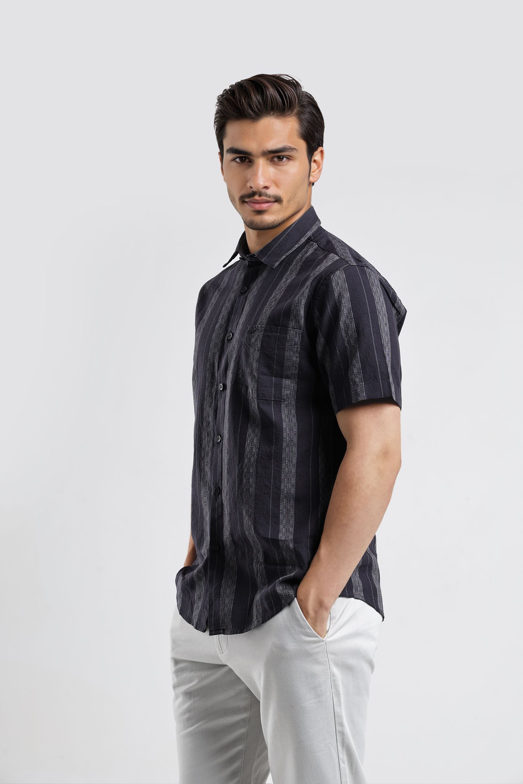 Man wearing a dark striped shirt and white pants on a light gray background