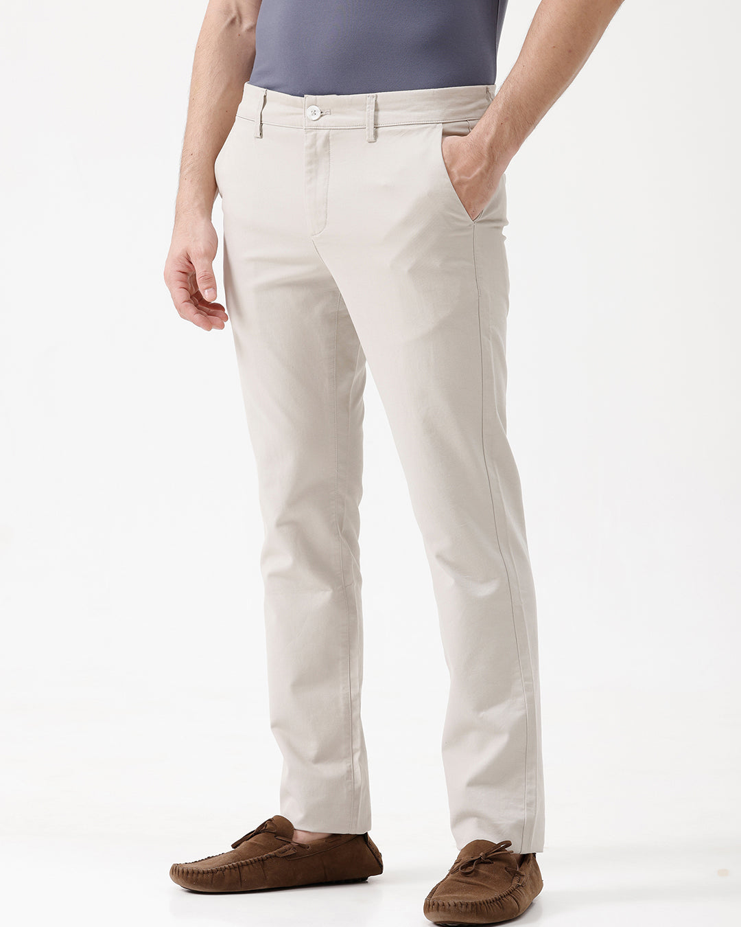 A person wearing light beige chino pants, a dark blue-gray t-shirt, and brown suede moccasin shoes, standing against a plain white studio background.