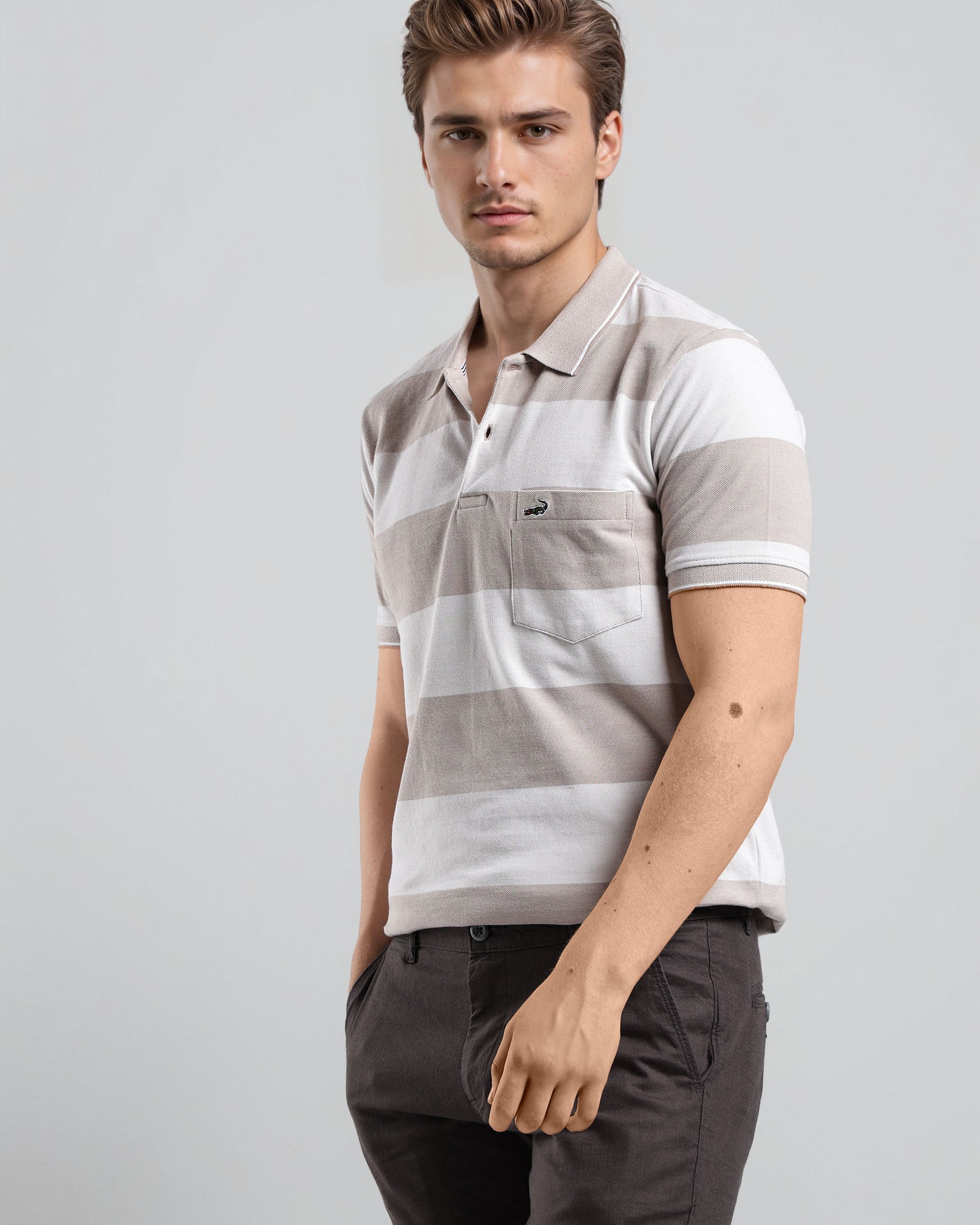 Man wearing a striped polo shirt and dark pants on a light gray background