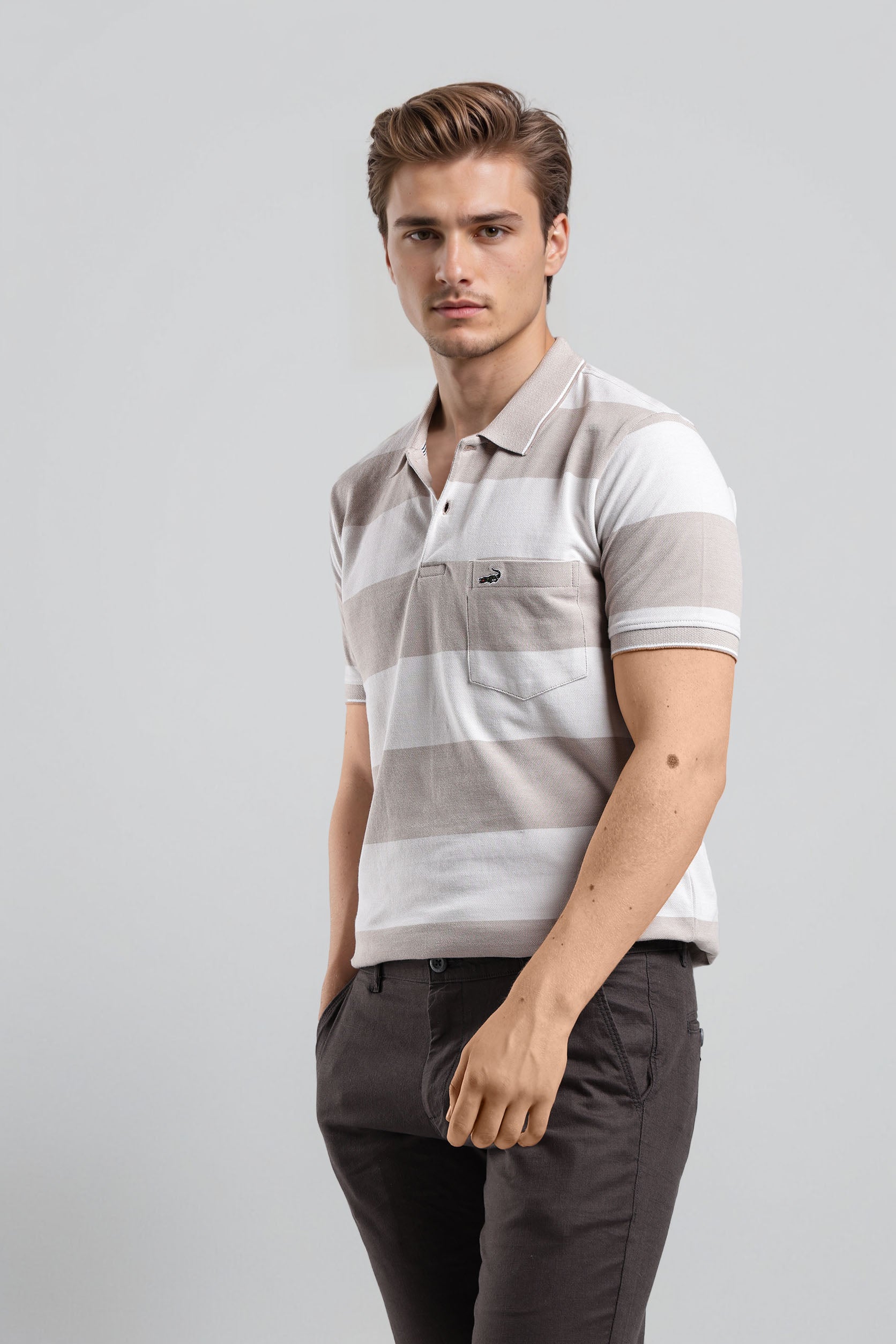 Man wearing a striped polo shirt and dark pants on a light gray background