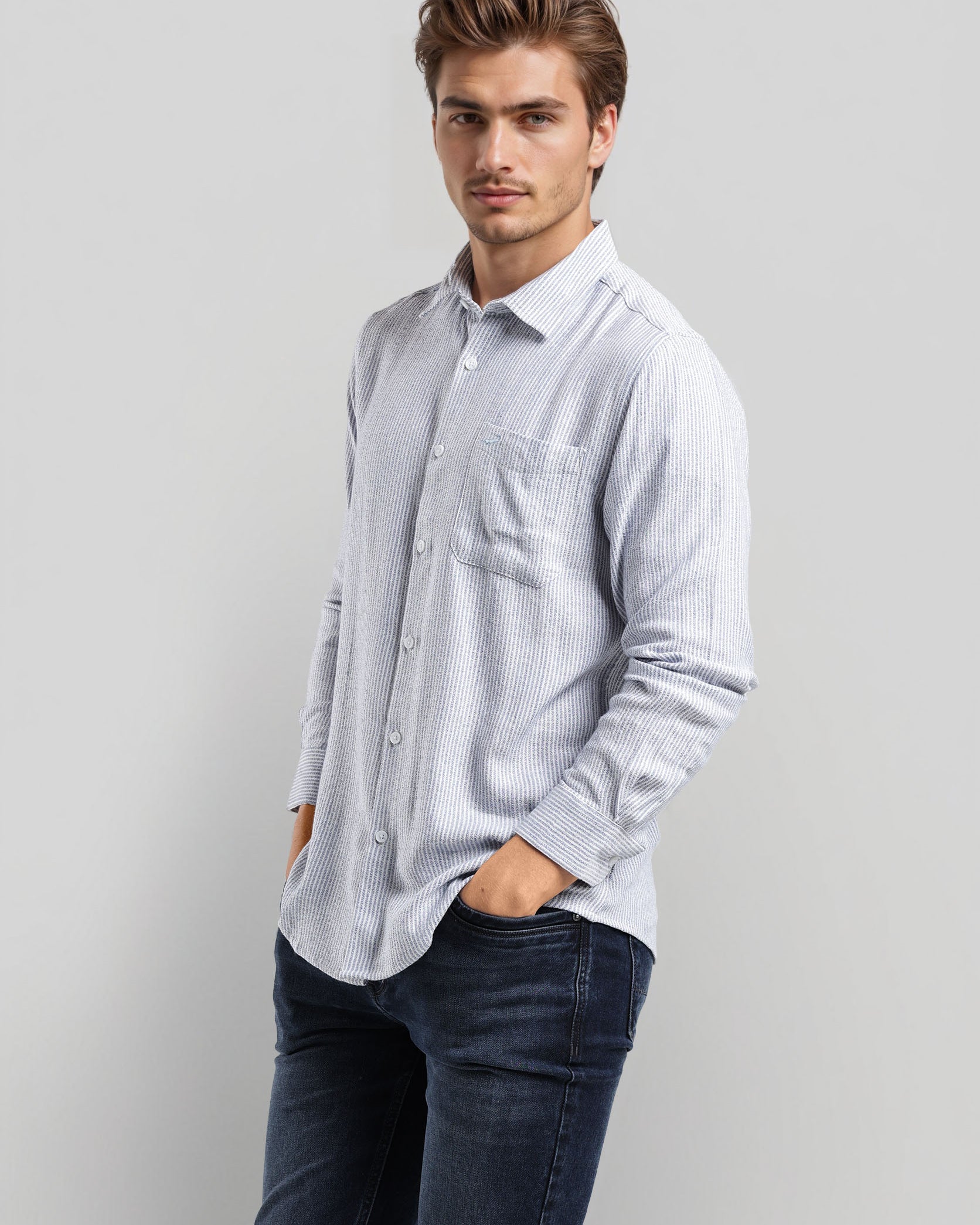 Man wearing a light blue striped shirt and dark jeans against a plain background