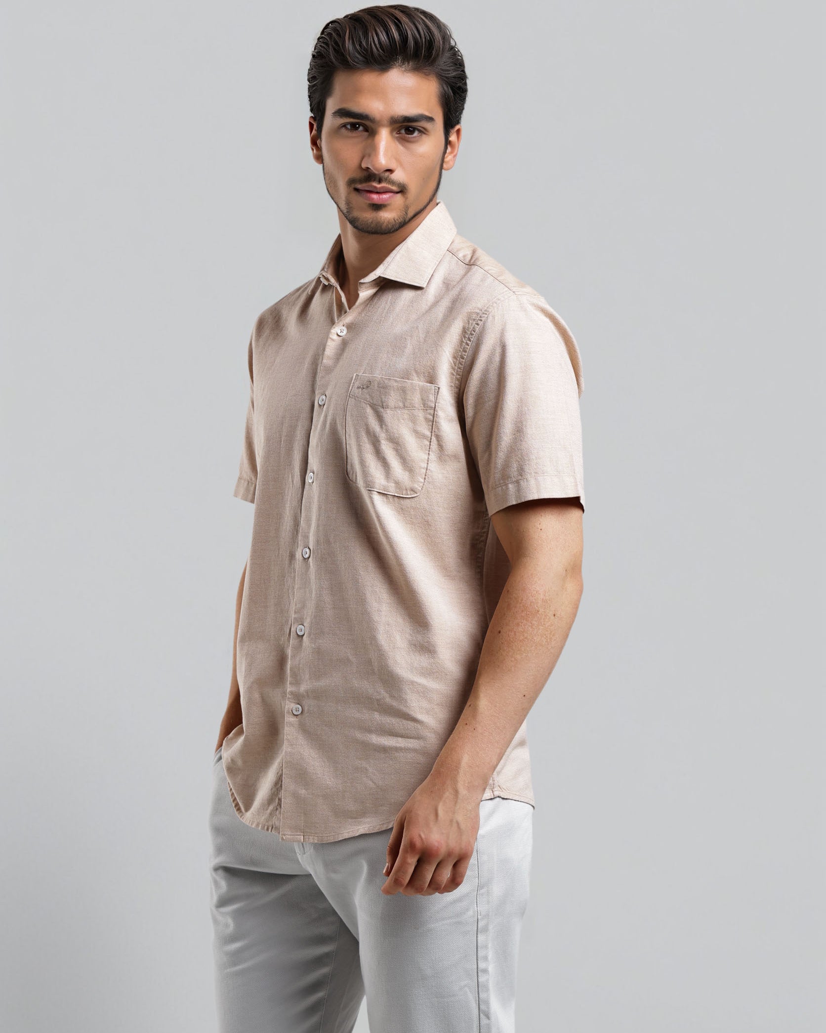 Man wearing a beige shirt and white pants against a gray background