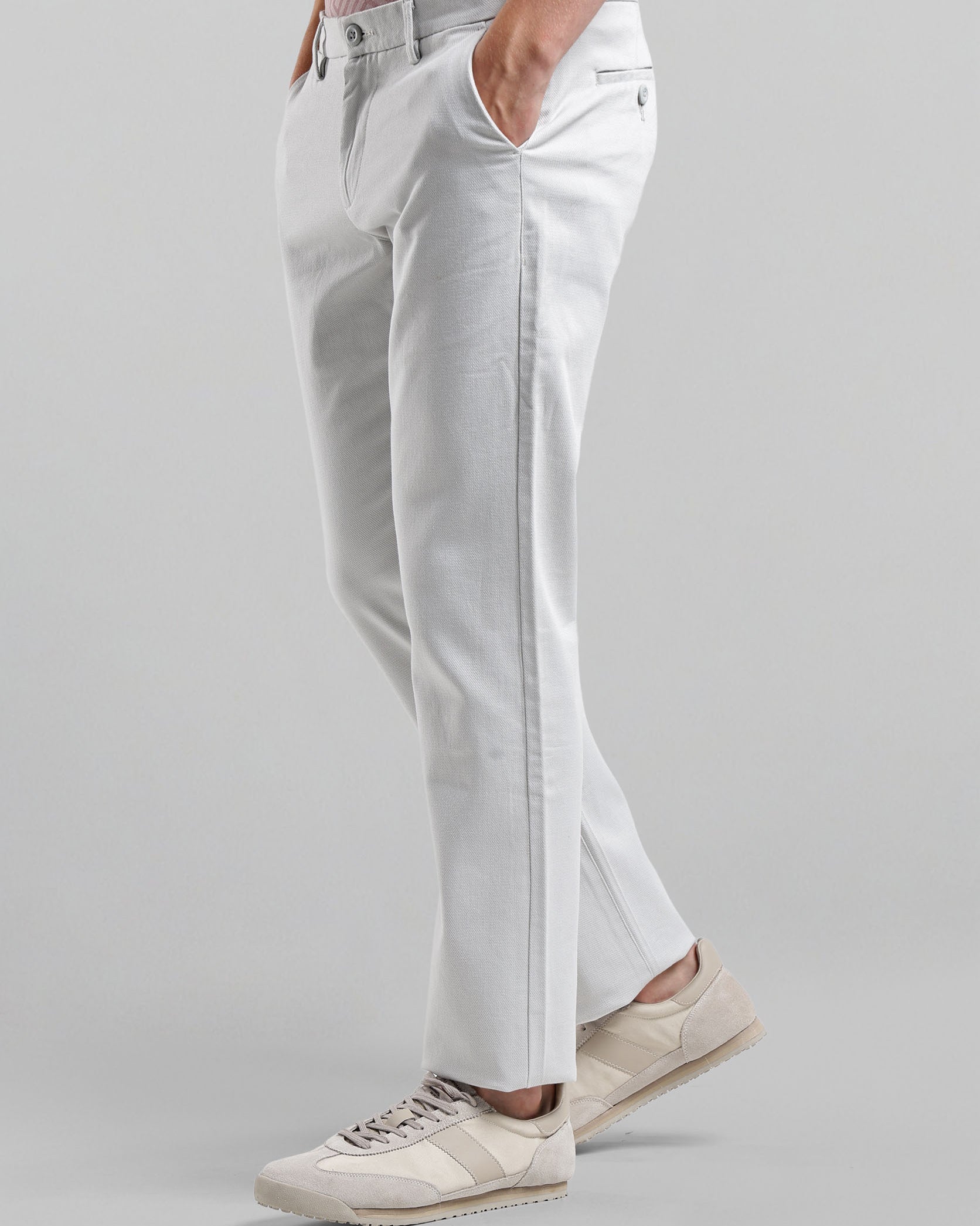 Person wearing light gray pants and beige sneakers on a plain background