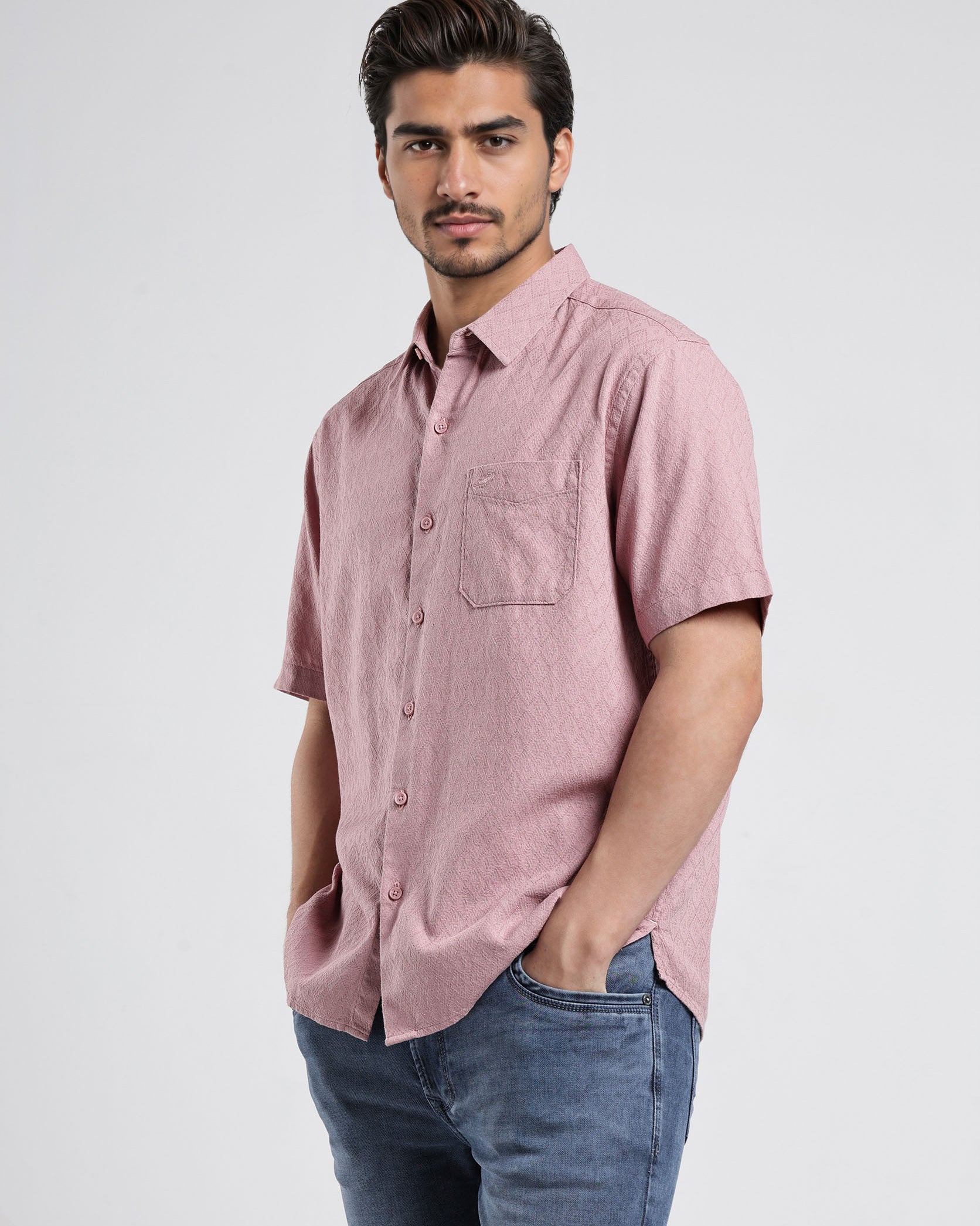 Man wearing a pink short-sleeve shirt and blue jeans on a white background