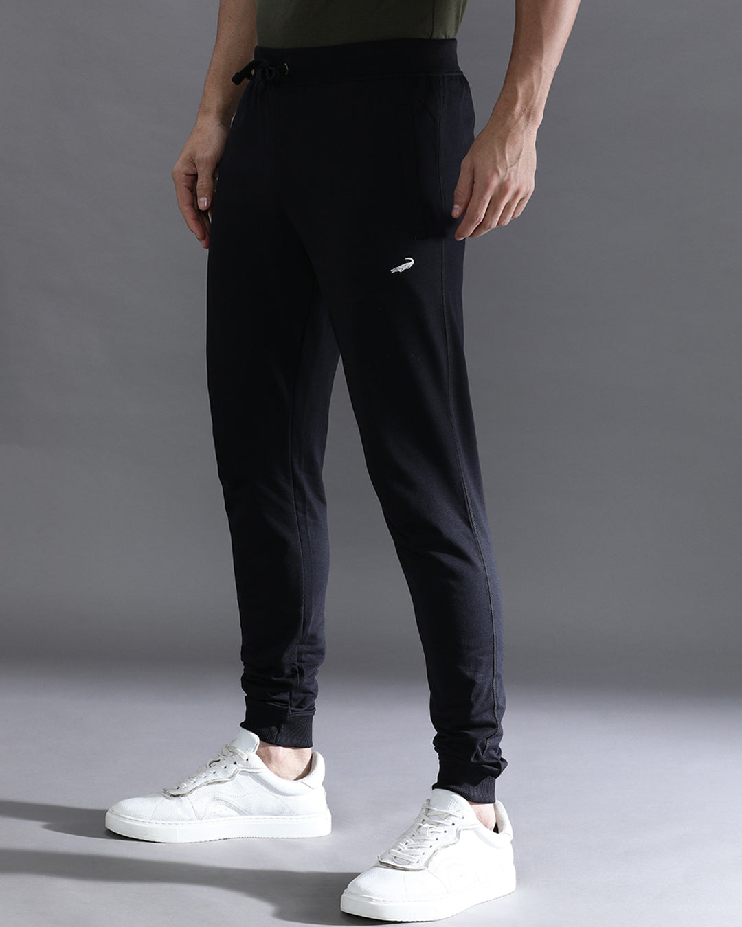 Person wearing black jogger pants and white sneakers on a gray background