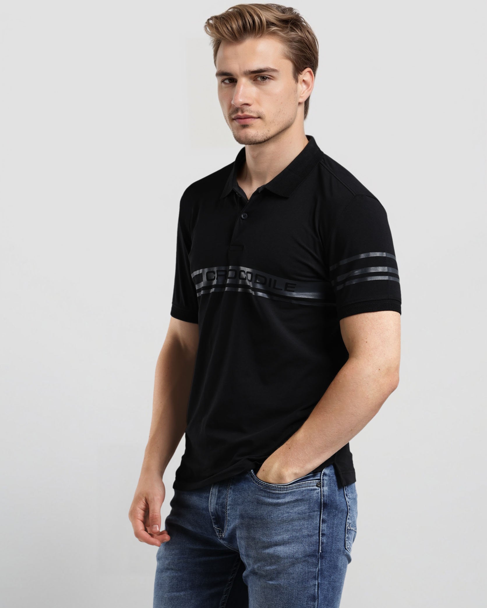 Man wearing a black polo shirt with white text and blue jeans on a light gray background