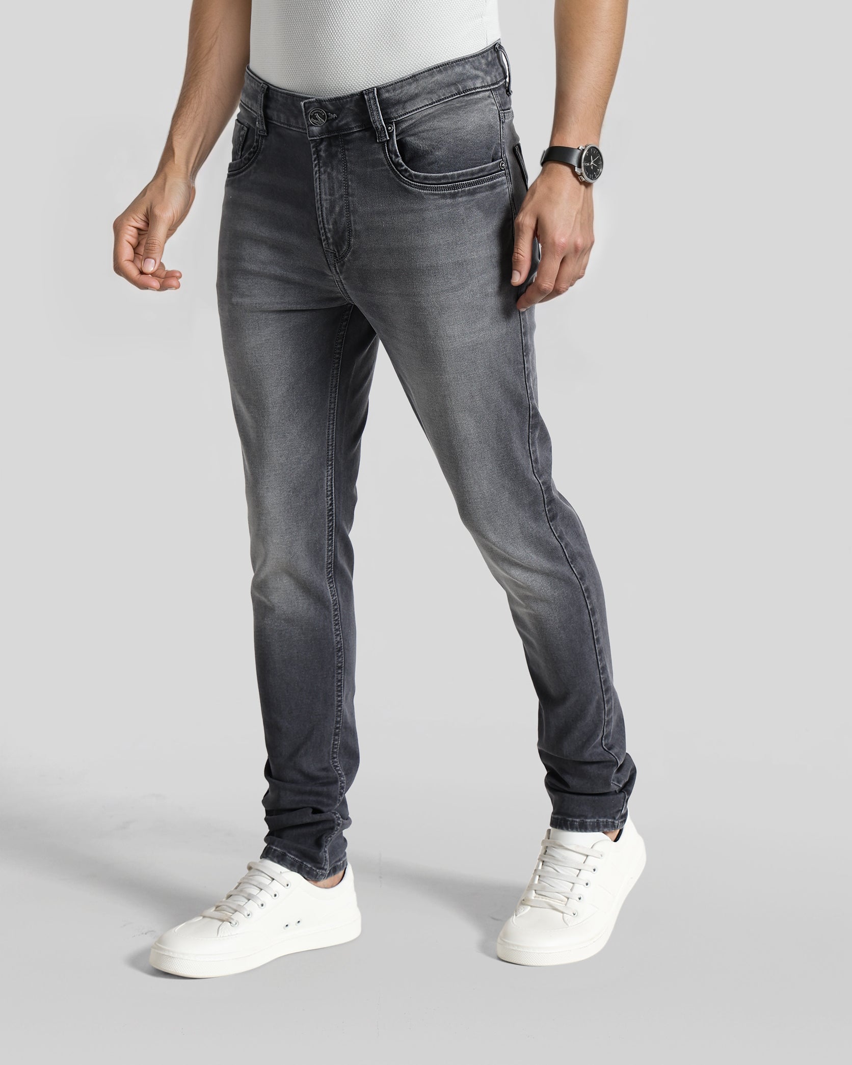 Person wearing gray jeans and white sneakers on a plain background