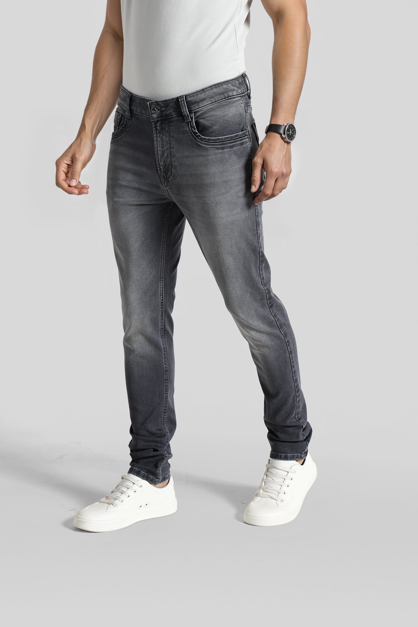 Person wearing gray jeans and white sneakers on a plain background