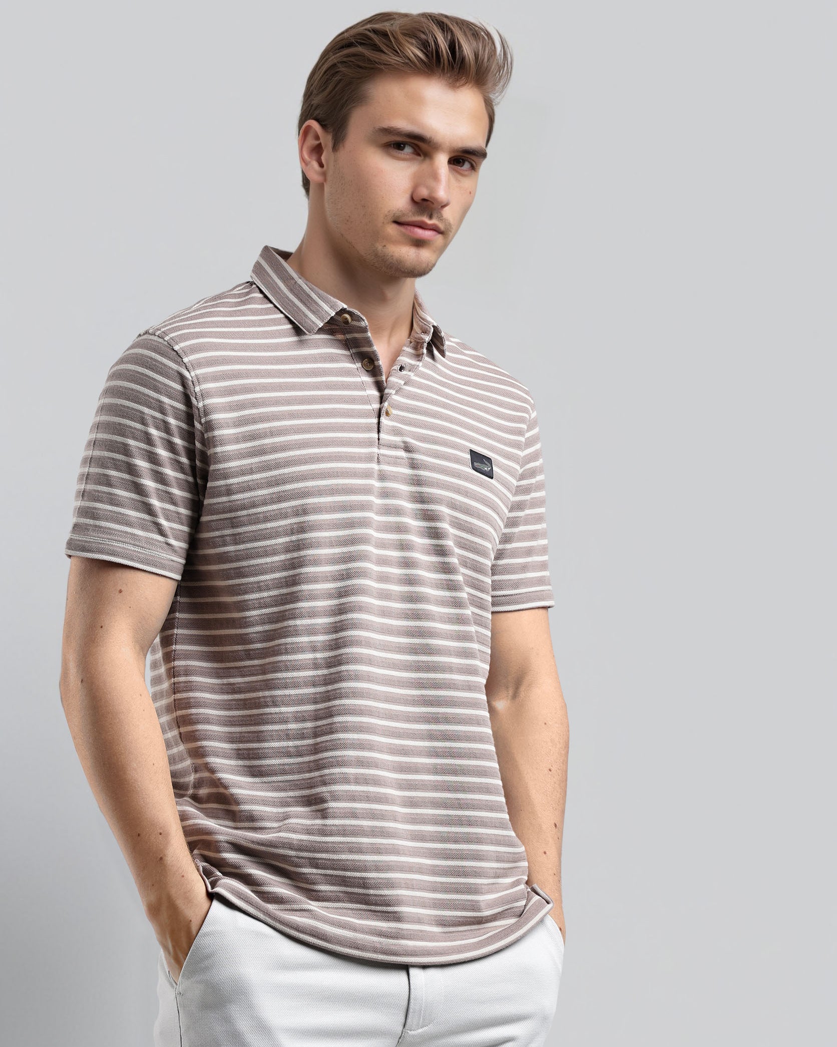 Man wearing a striped polo shirt and light pants on a gray background