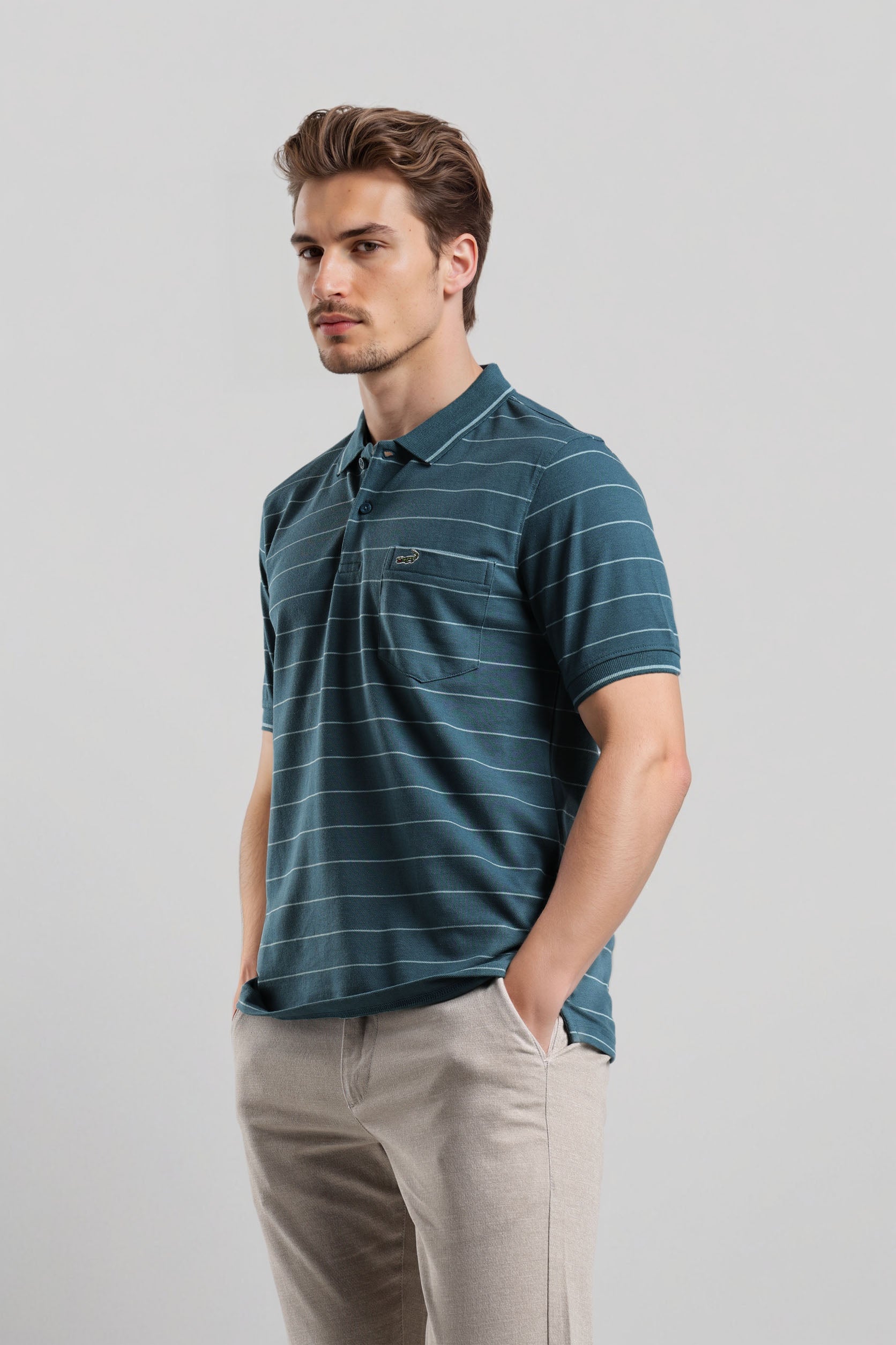 Man wearing a blue striped polo shirt and beige pants against a light gray background