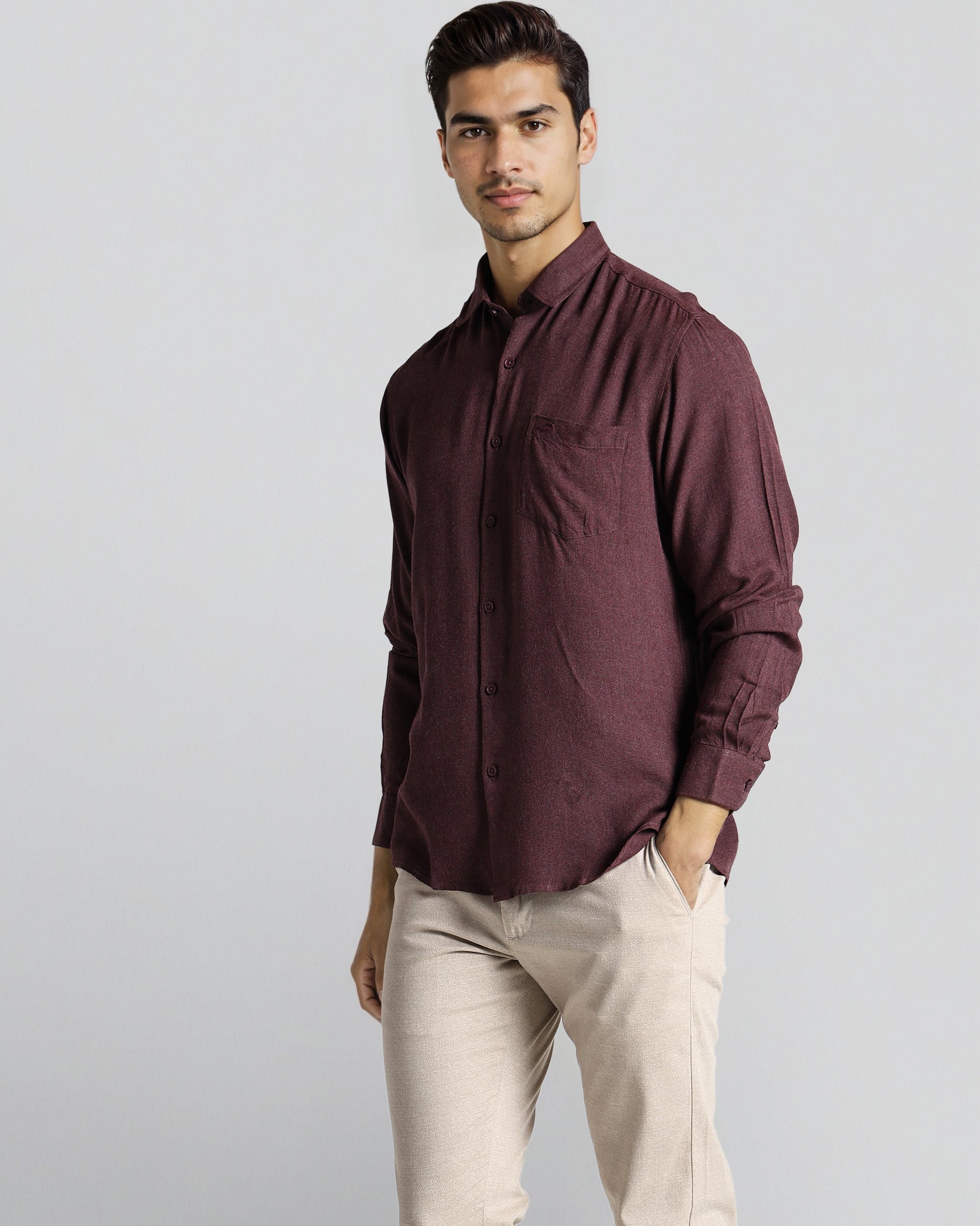 Man wearing a maroon shirt and beige pants on a light gray background