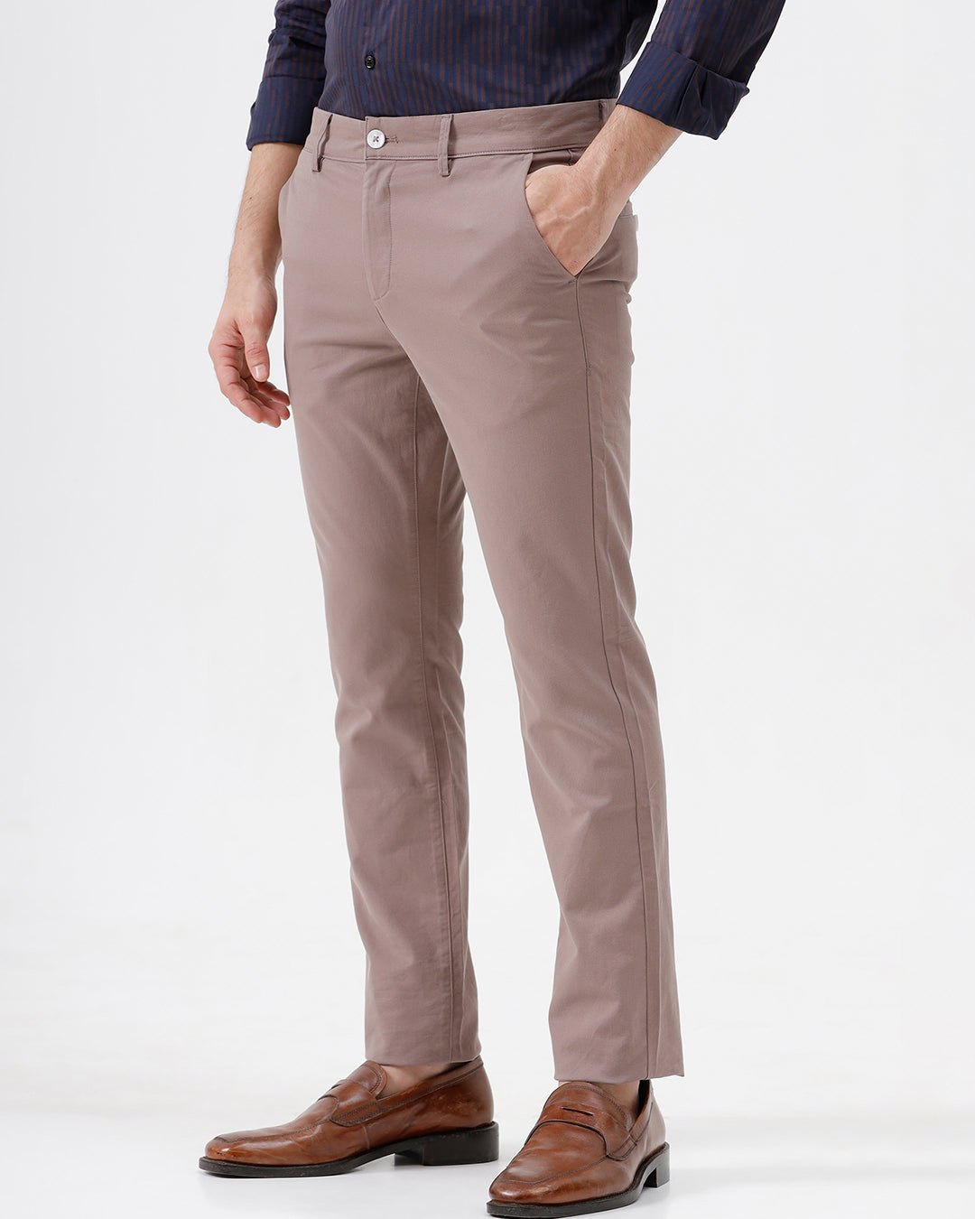 A person wearing slim-fit taupe trousers, a navy blue striped button-down shirt, and brown leather loafers, standing against a plain white studio background.