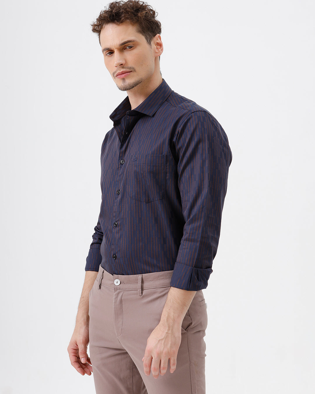 A man wearing a dark navy blue button-down shirt with thin vertical red stripes and light brown trousers, standing against a plain white studio background.