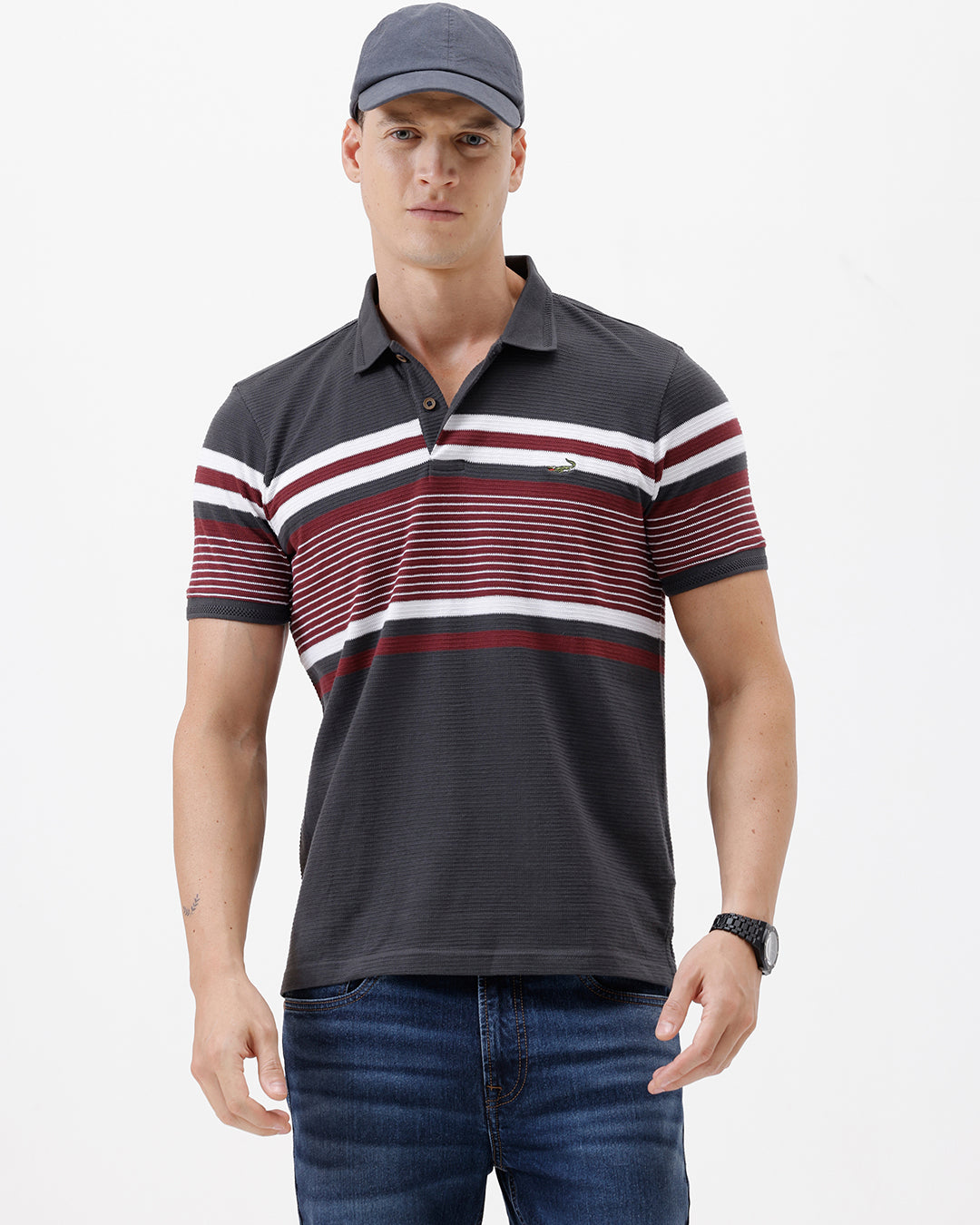 A man wearing a dark gray Lacoste polo shirt with horizontal red and white stripes across the chest and sleeves, paired with blue jeans, against a plain light gray background.