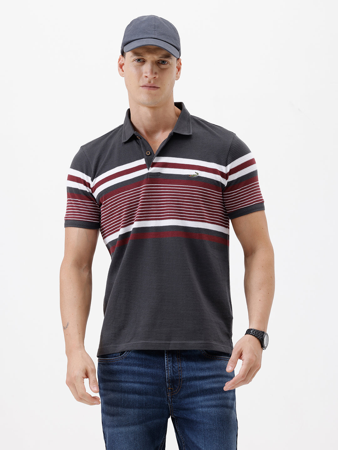 A man wearing a dark gray Lacoste polo shirt with horizontal red and white stripes across the chest and sleeves, paired with blue jeans, against a plain light gray background.