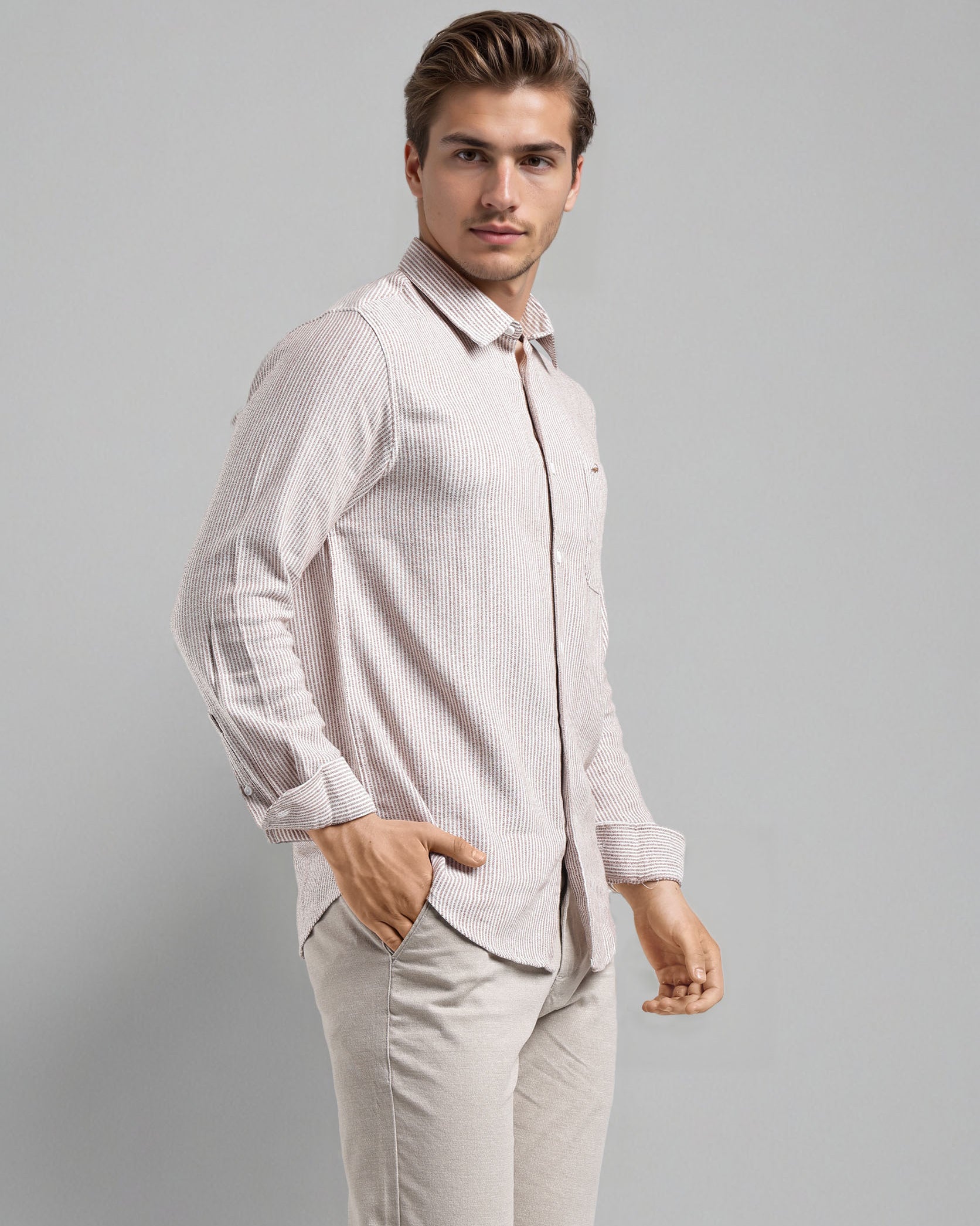Man wearing a light pink shirt and beige pants against a gray background