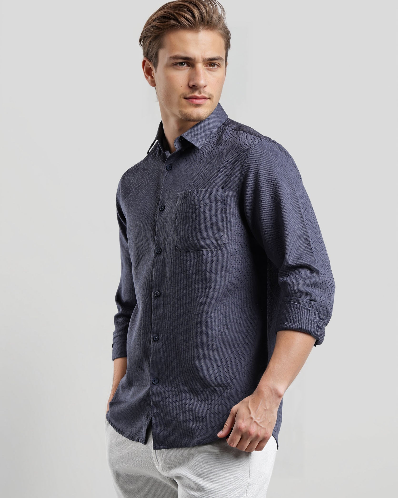 Man wearing a dark blue button-up shirt and light gray pants on a white background