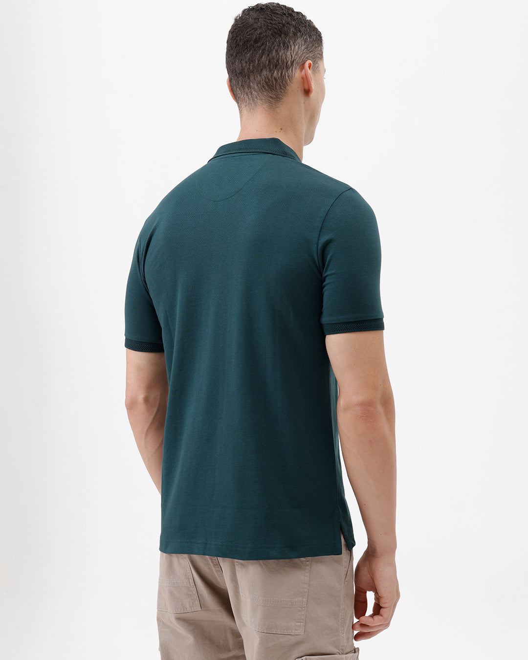 A man wearing a dark teal short-sleeve polo shirt with a chest pocket, paired with beige cargo pants, standing against a plain white studio background.