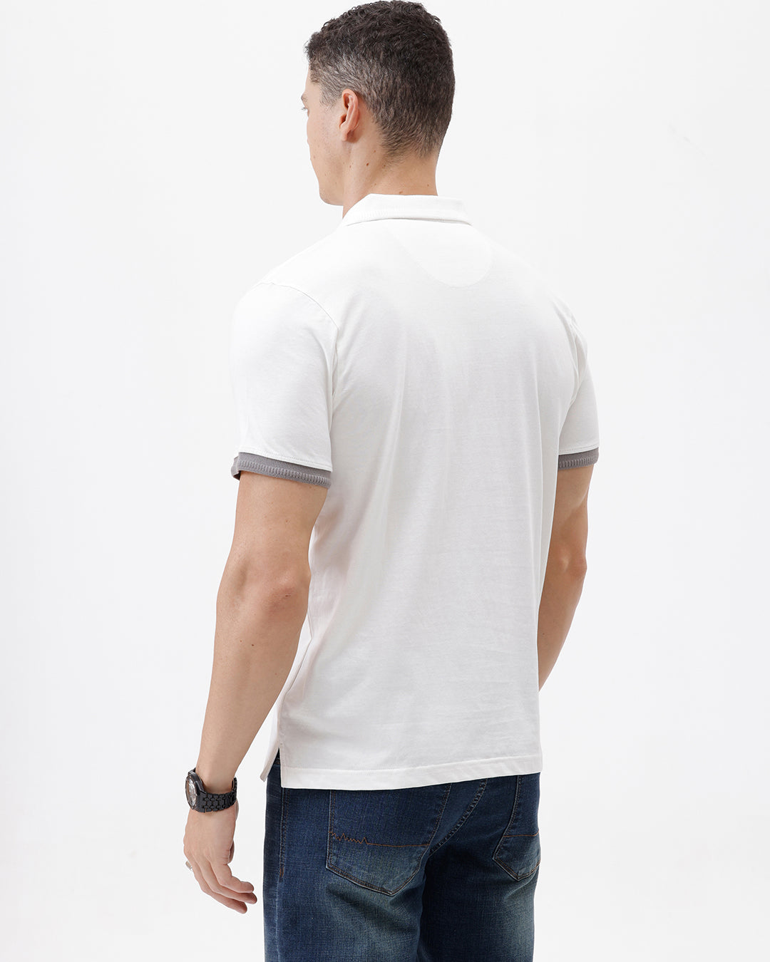 A man wearing a white short-sleeve polo shirt with gray ribbed trim on the collar and sleeve cuffs, paired with dark blue jeans, photographed against a plain white studio background.