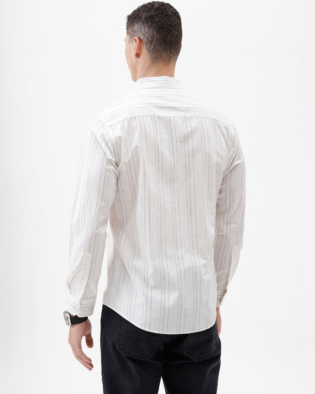 A man wearing a white long-sleeve button-up shirt with thin vertical gray stripes and black pants, standing against a plain white studio background.