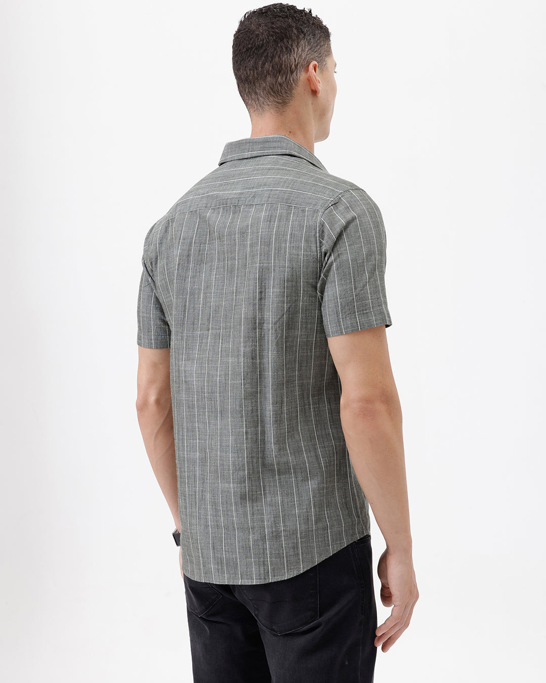 A man wearing a short-sleeve button-up shirt with a gray and white vertical stripe pattern, paired with black pants, standing against a plain white studio background.