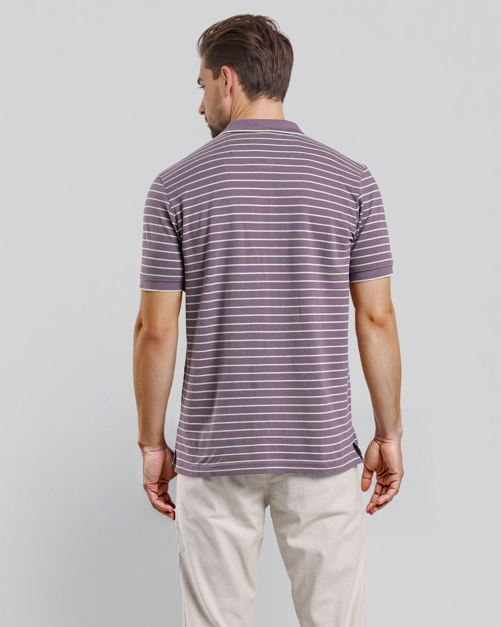 Man wearing a striped polo shirt and light-colored pants on a plain background