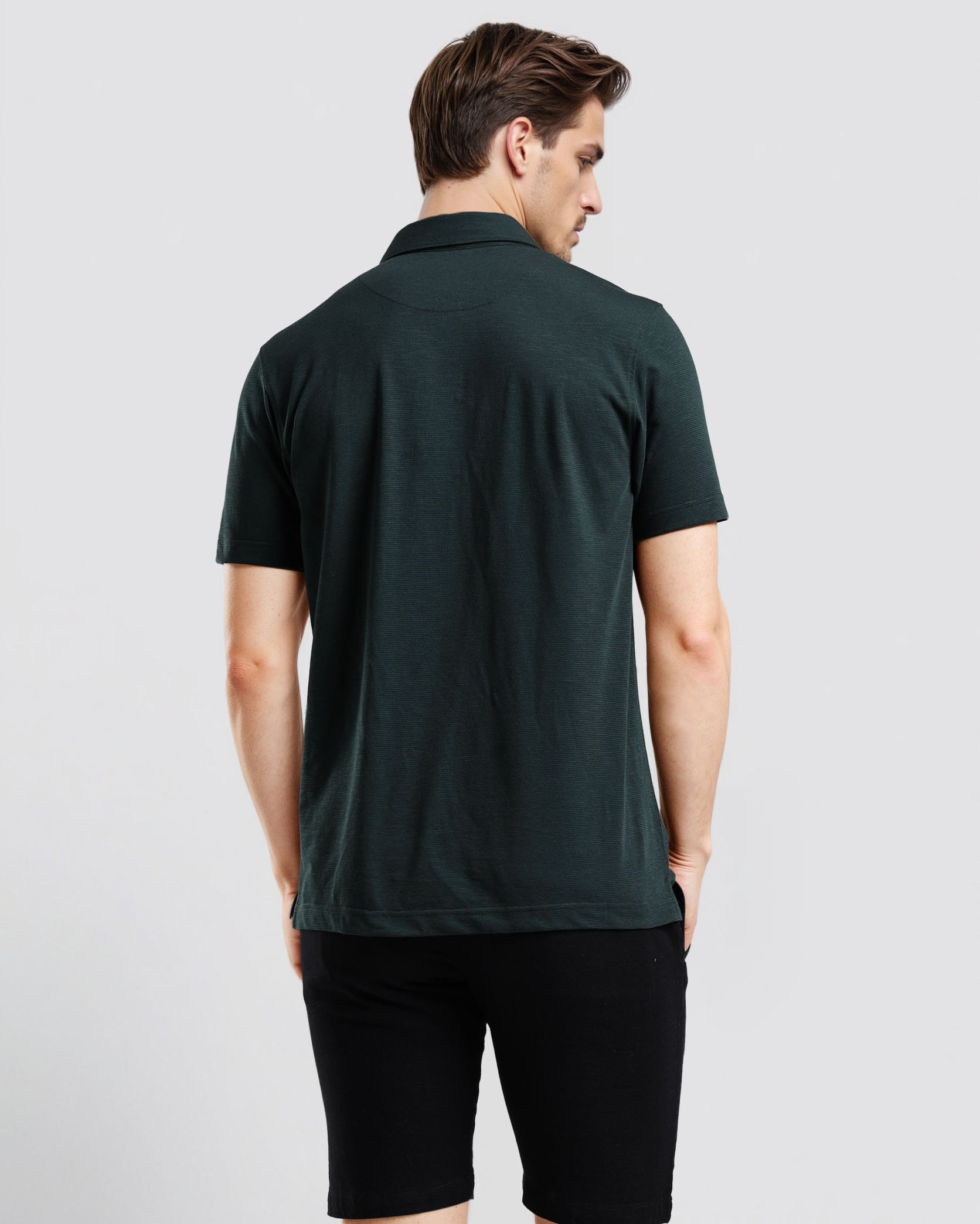 Man wearing a dark green polo shirt and black shorts on a light gray background