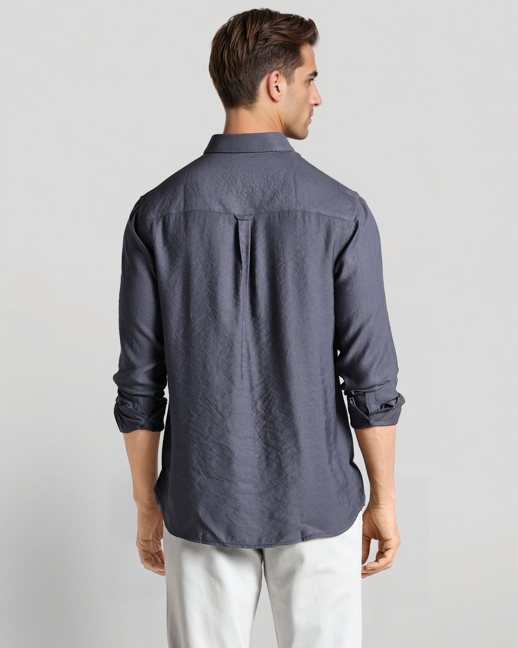 Man wearing a dark gray button-up shirt and white pants on a light gray background