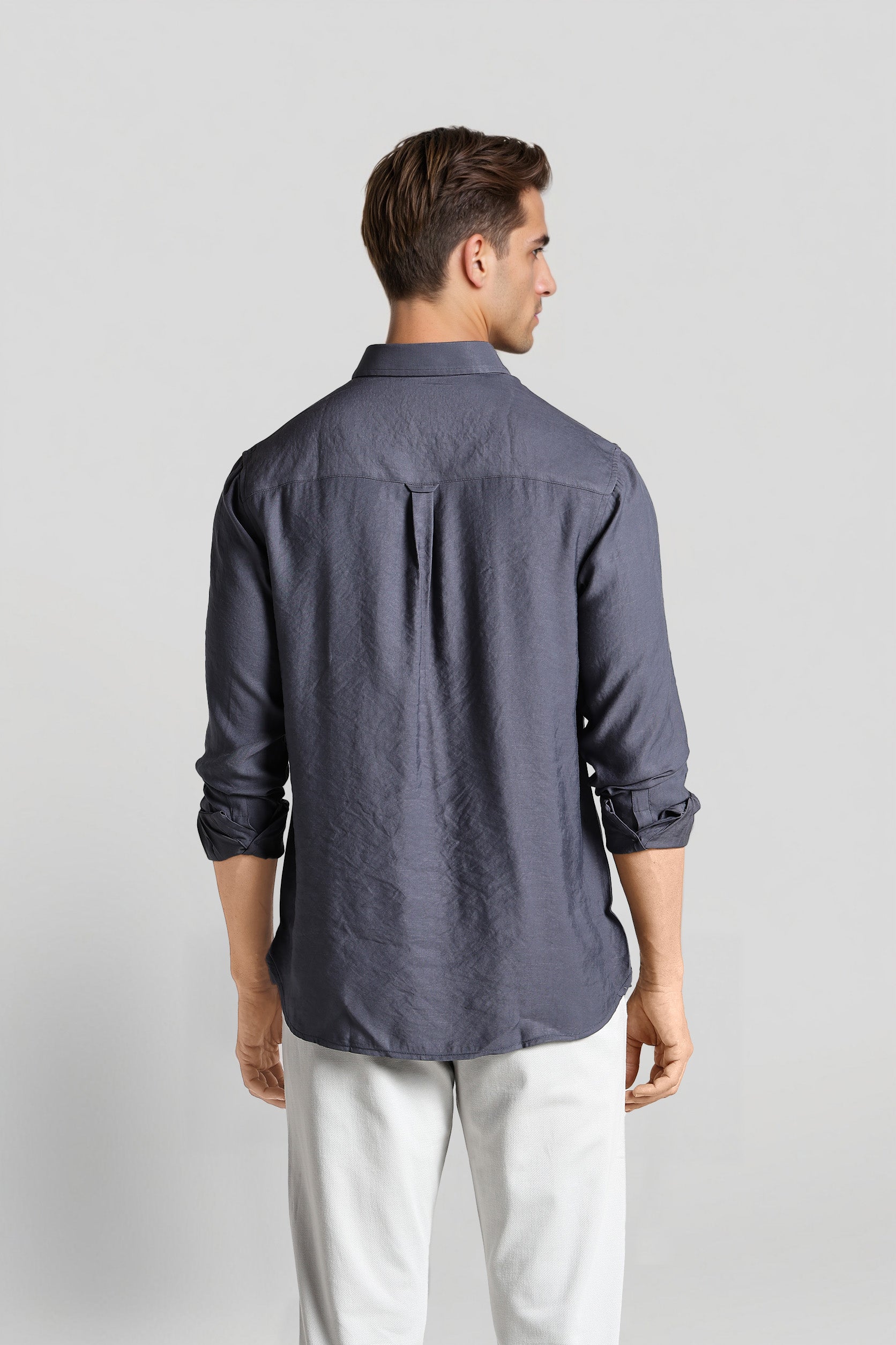 Man wearing a dark gray button-up shirt and white pants on a light gray background