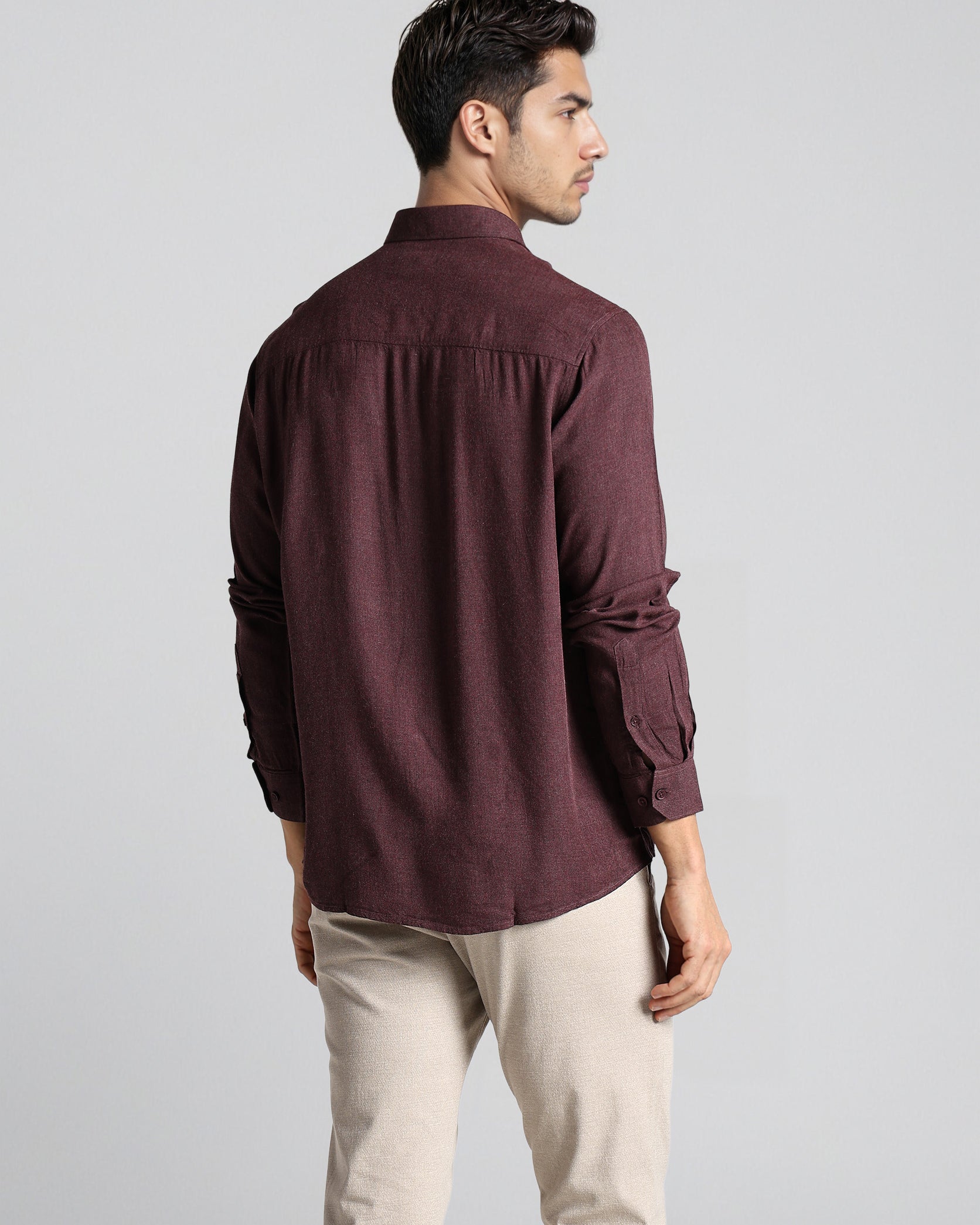 Man wearing a maroon shirt and beige pants on a light gray background