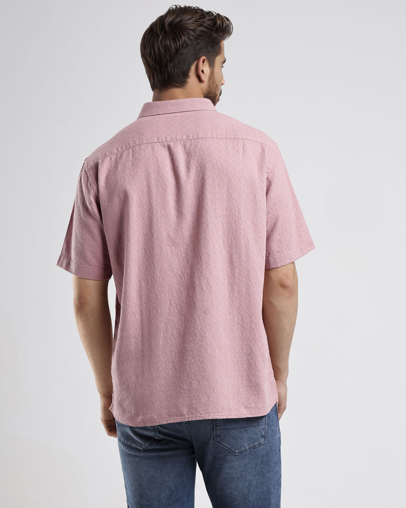 Man wearing a pink short-sleeve shirt and blue jeans on a white background