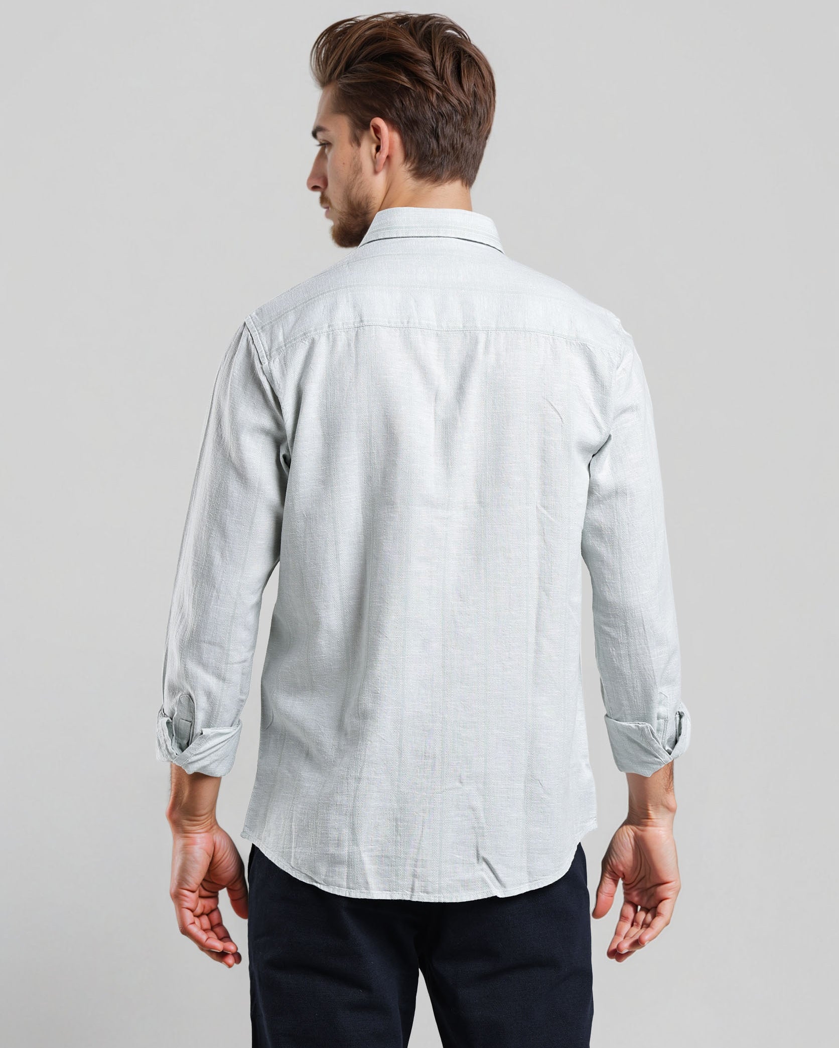 Man wearing a light-colored shirt with rolled-up sleeves on a plain background