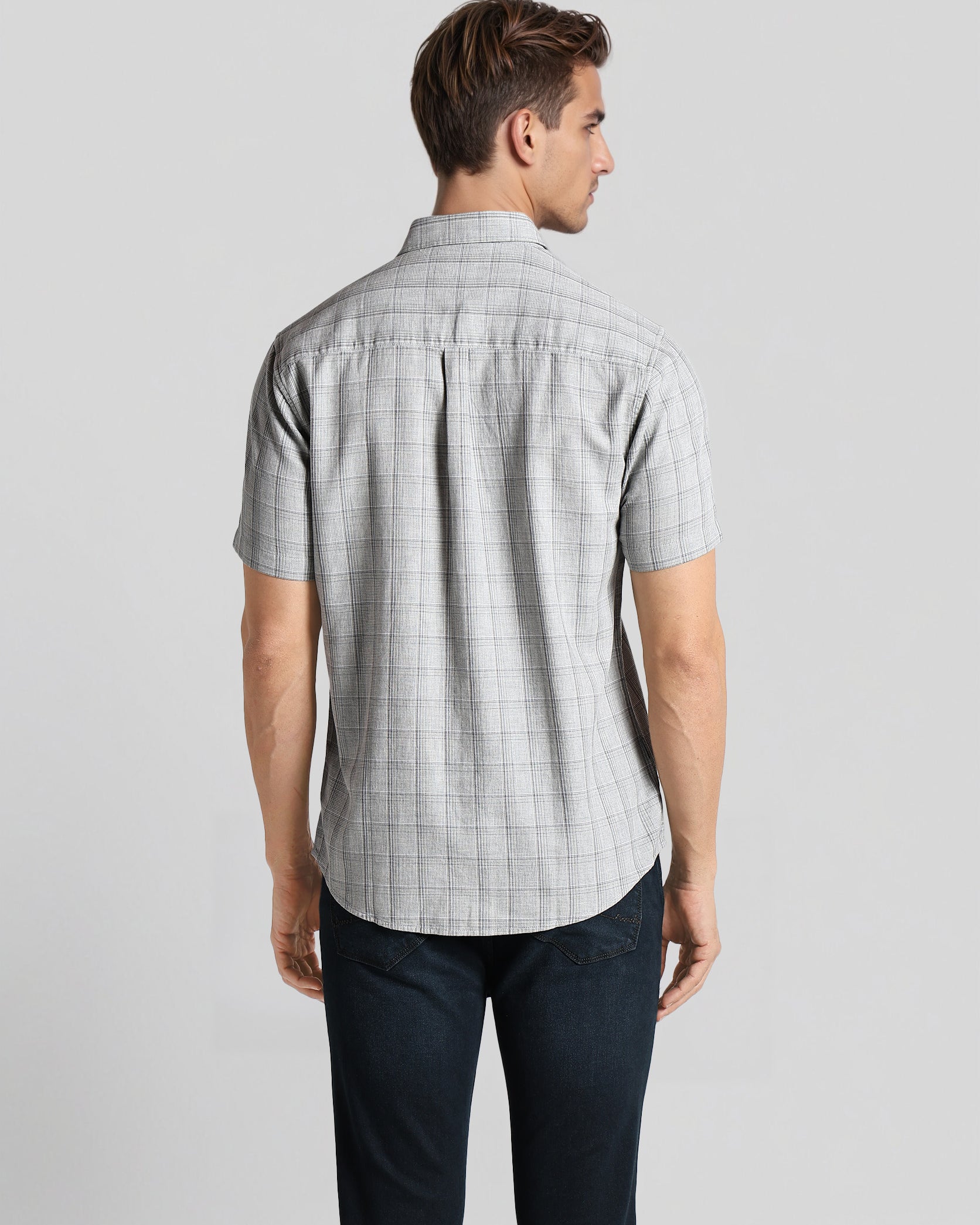 Man wearing a gray checkered shirt and dark pants on a light gray background