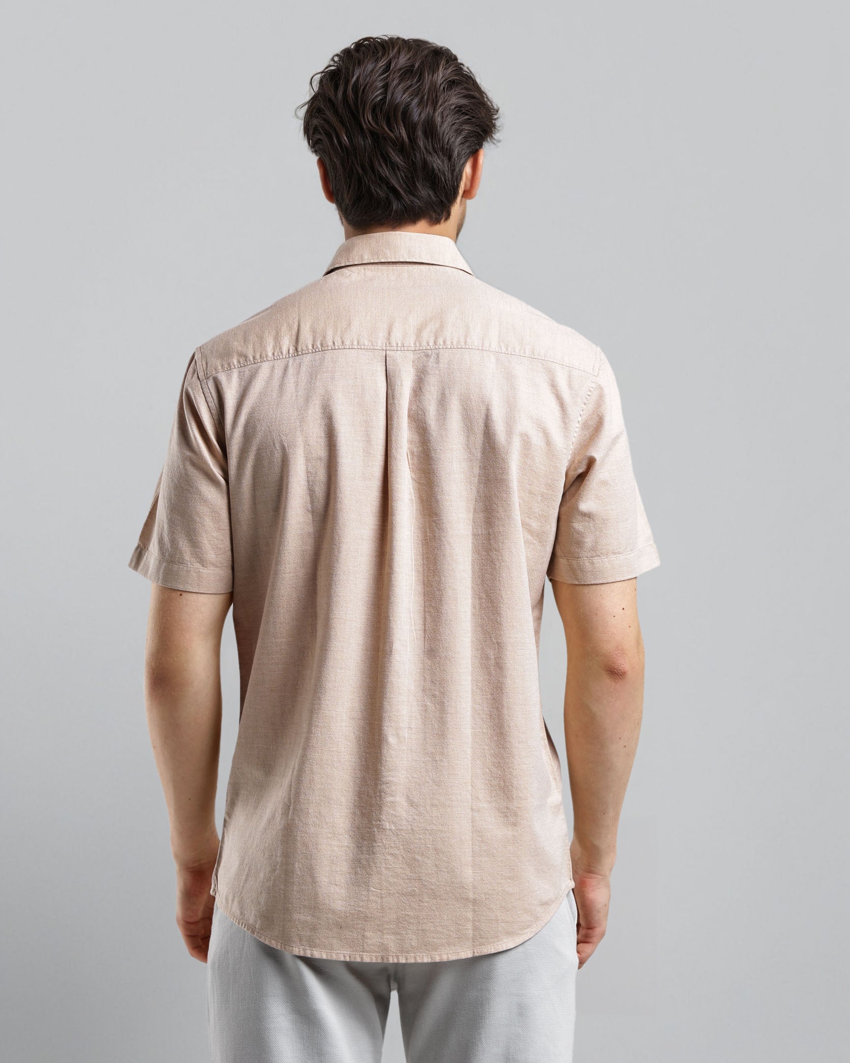 Man wearing a beige short-sleeve shirt and light gray pants against a plain background