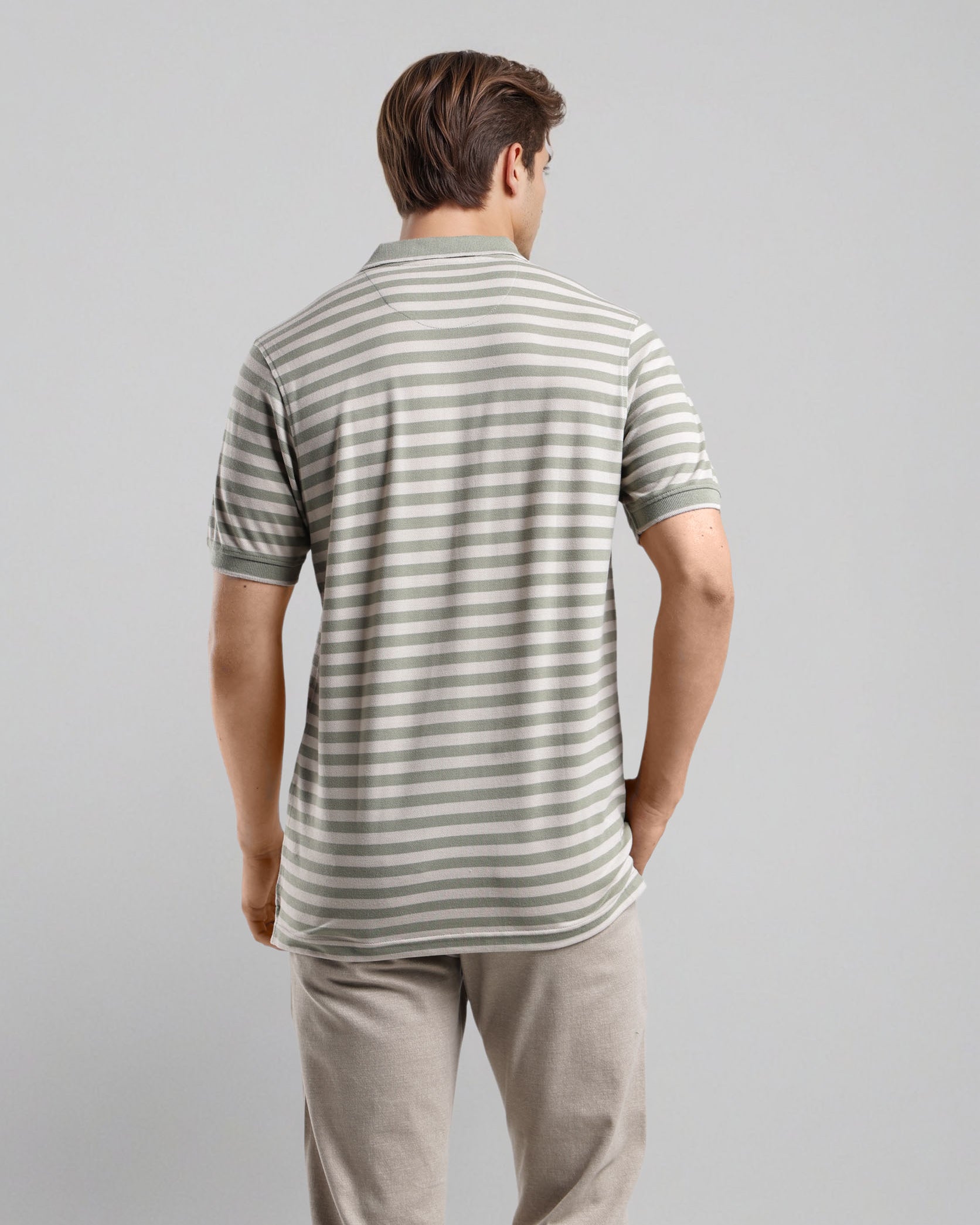 Man wearing a striped polo shirt and beige pants on a gray background