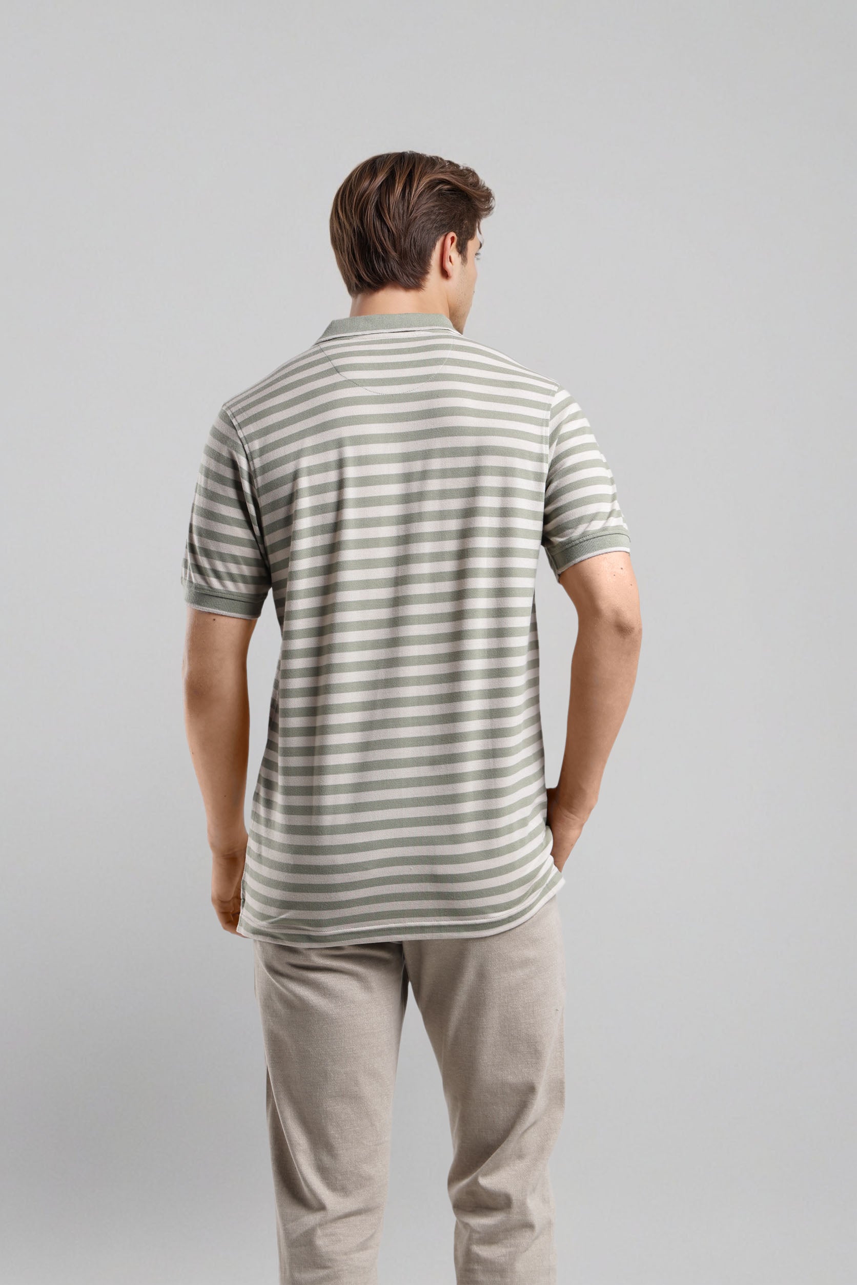 Man wearing a striped polo shirt and beige pants on a gray background