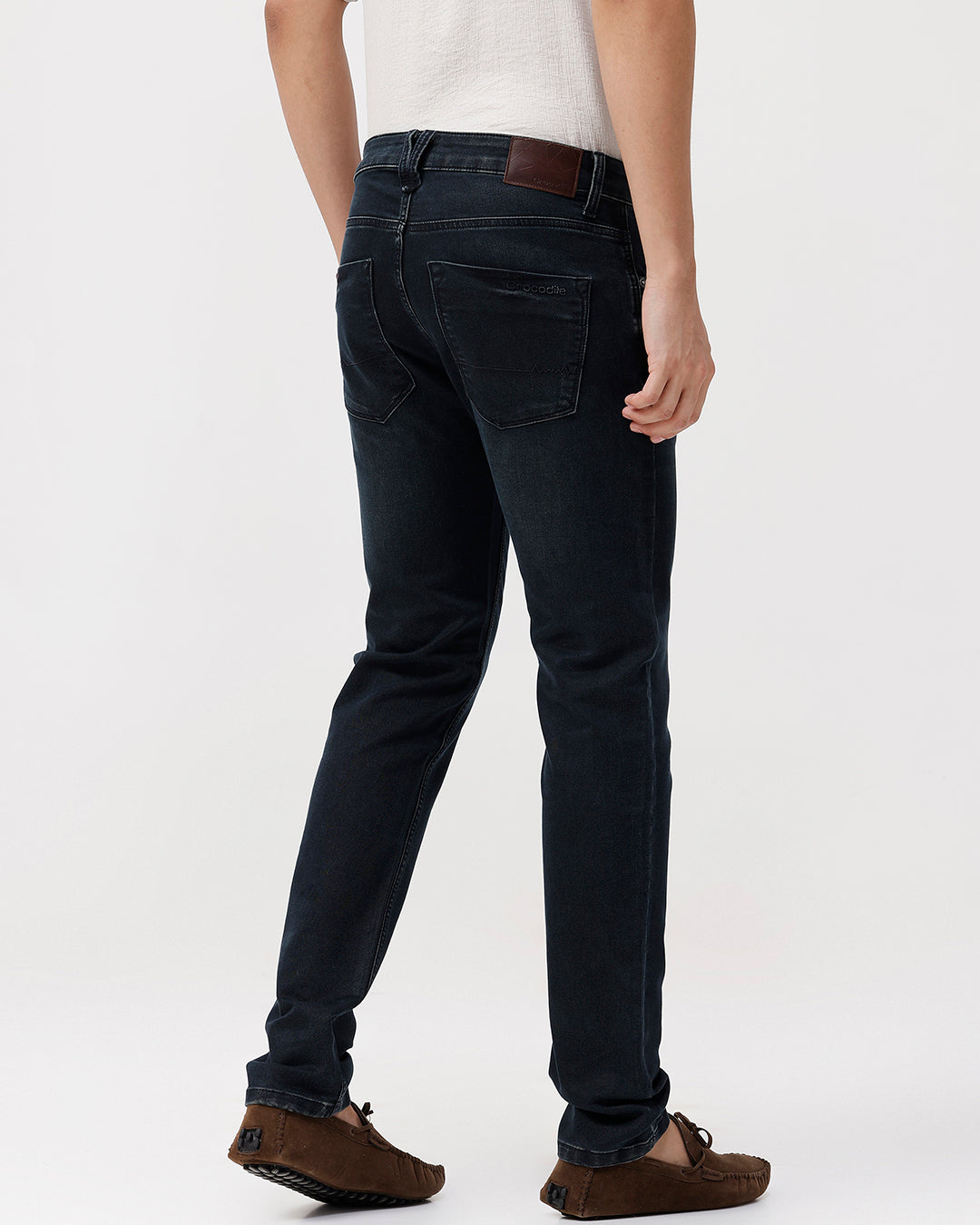 Person wearing black jeans and brown shoes on a white background
