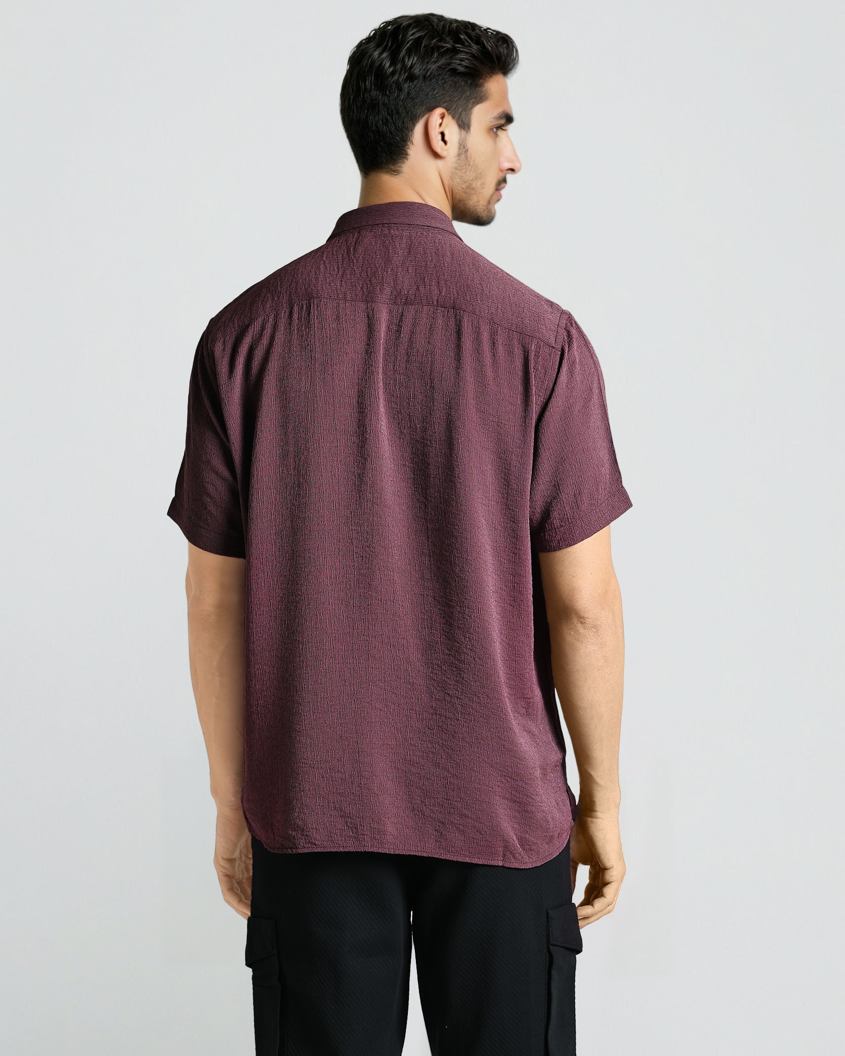 Man wearing a maroon shirt and black pants on a white background