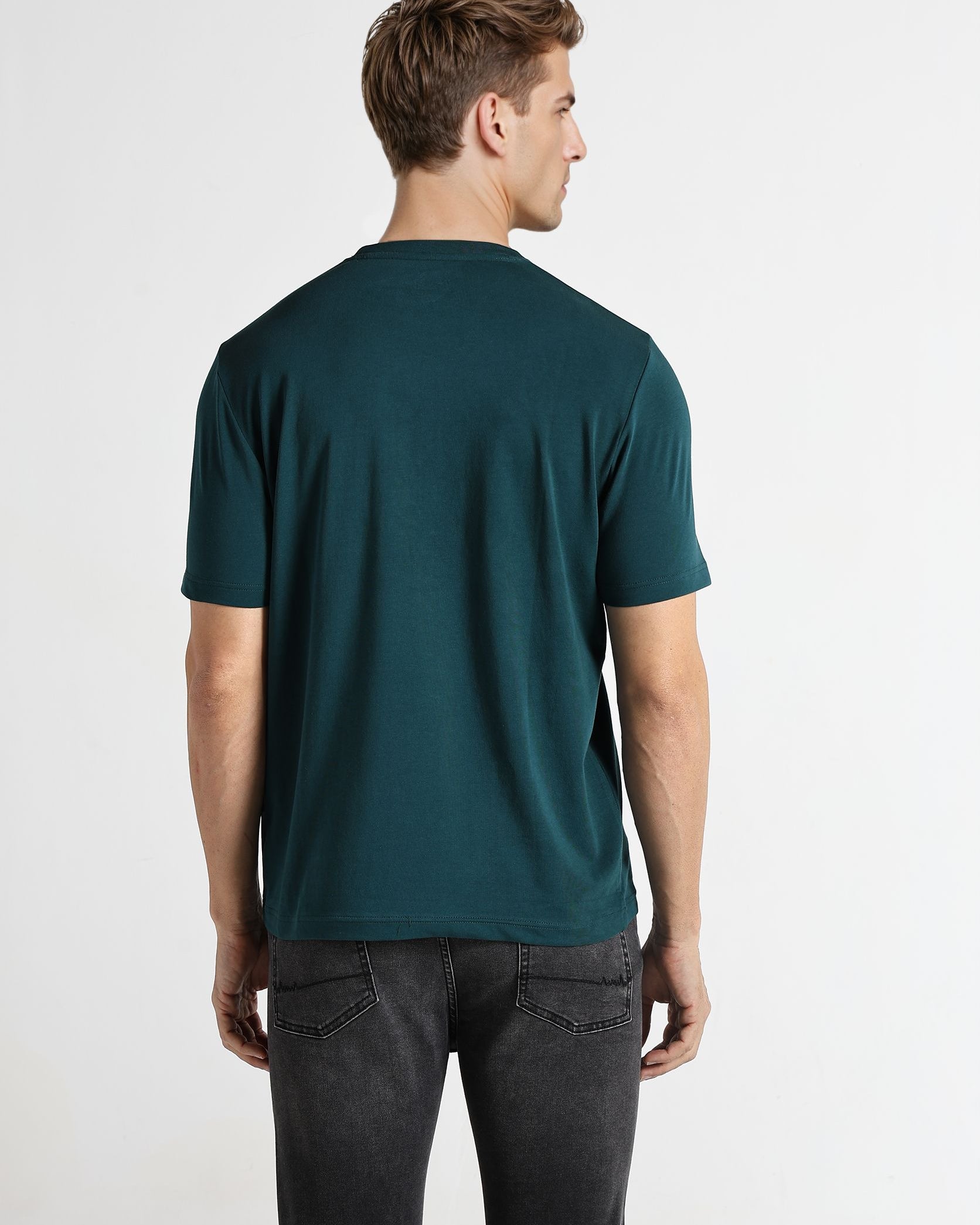 Man wearing a teal t-shirt and dark jeans on a white background